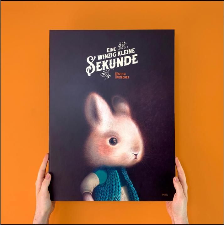 Buchcover mit dem Titel "Eine winzig kleine Sekunde" und einem Hasen. Hände halten das Buch vor orangefarbenem Hintergrund.