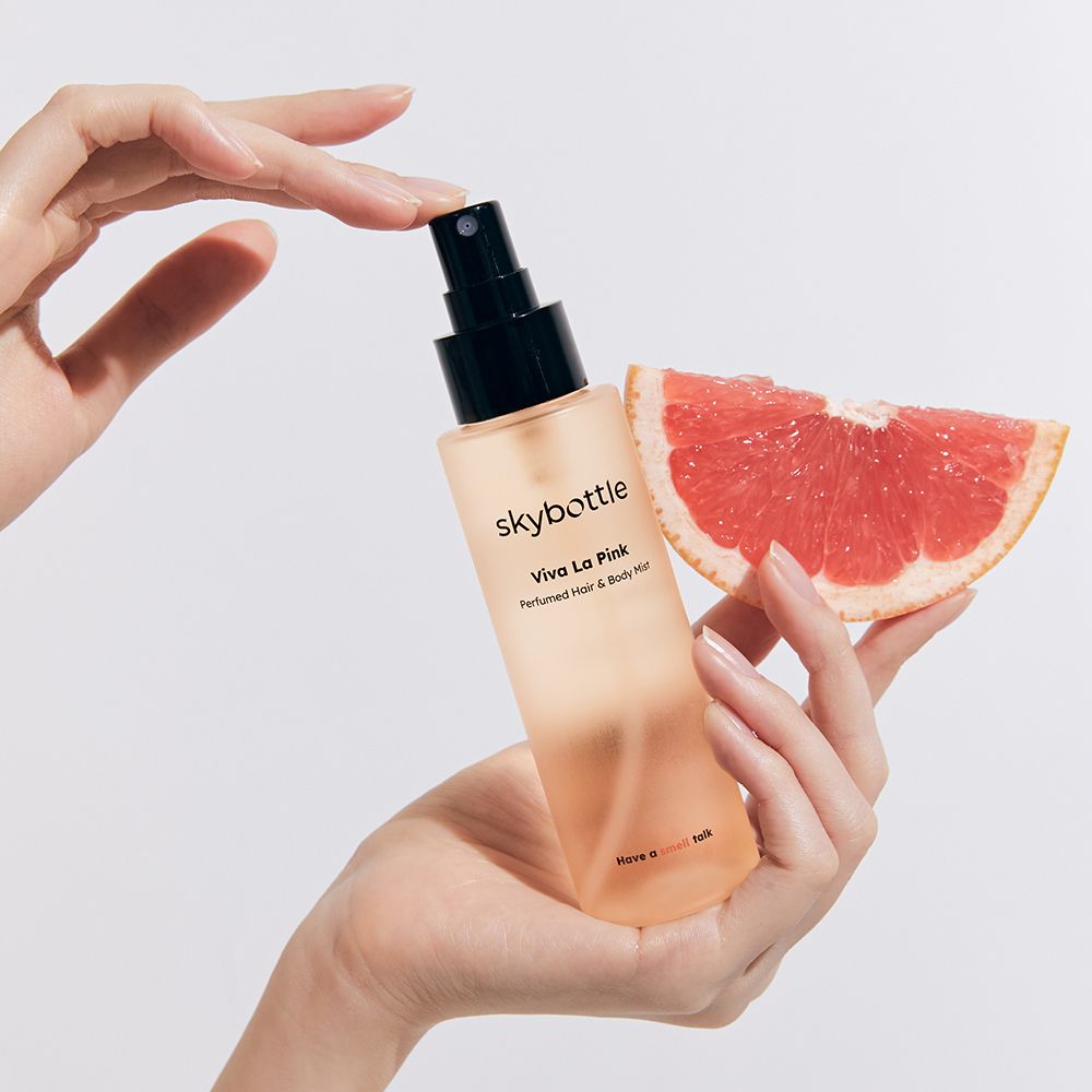 SKYBOTTLE Viva La Pink Hair & Body Mist. Flasche und Grapefruit-Hälfte. Hände.