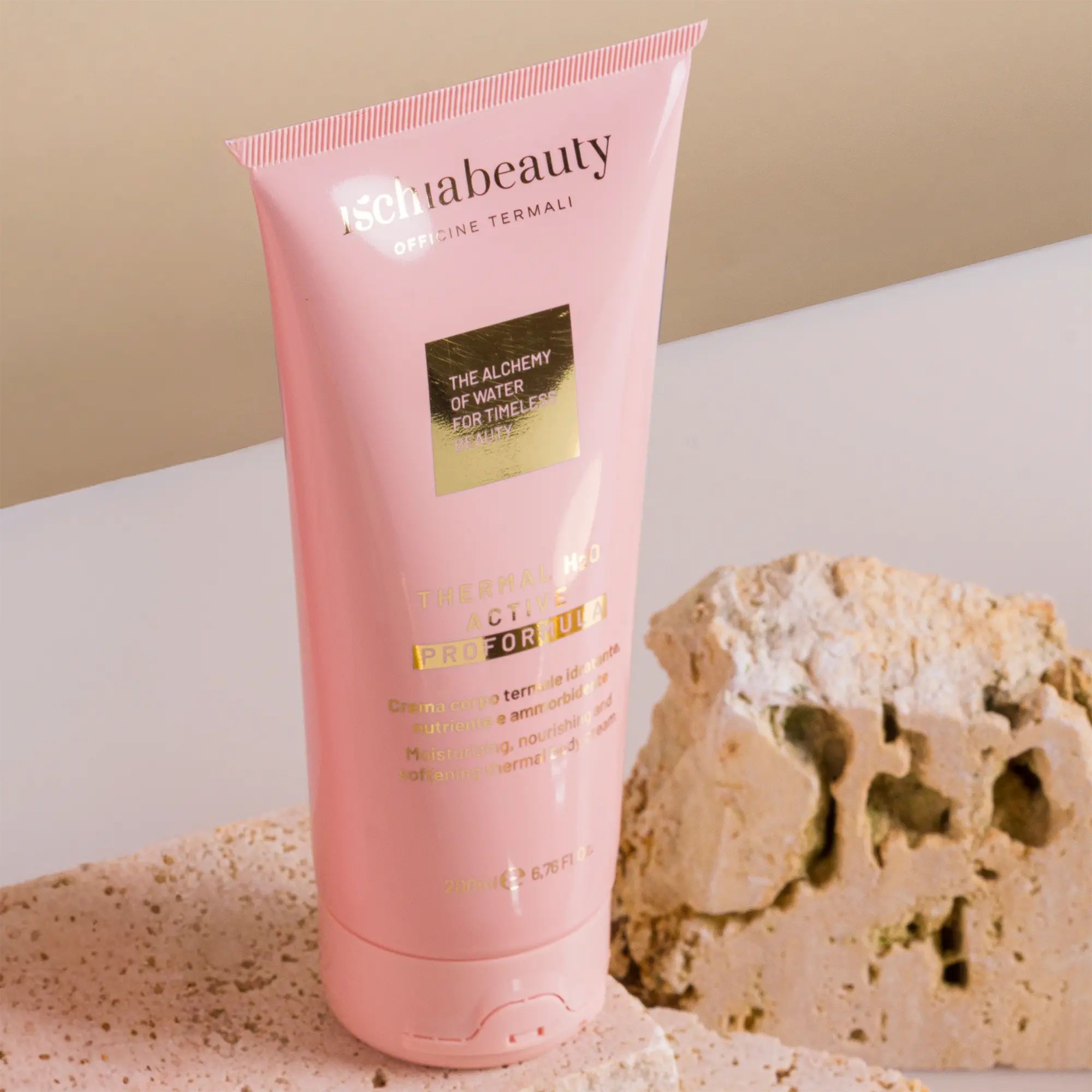 Rosa Tube mit Produkttext. Aufschrift: ischiabeauty, Thermal H2O Active Pro Formula. Neben Stein platziert.