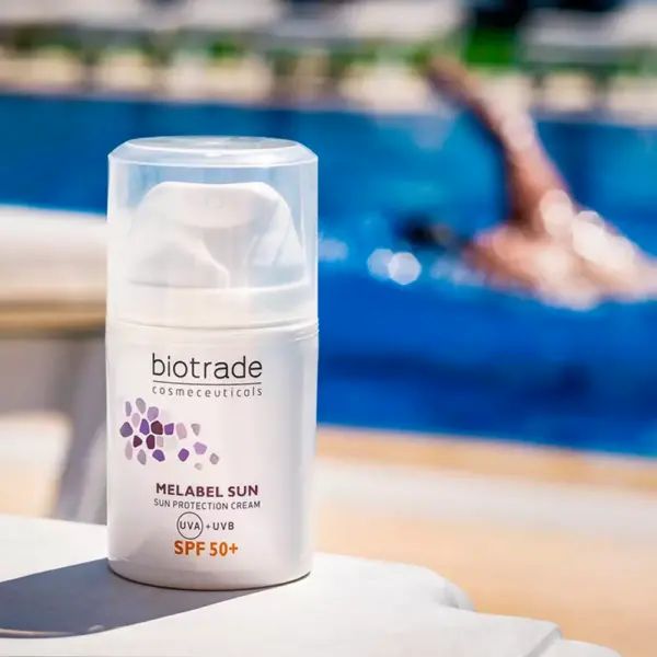 Weiße Flasche mit Pumpverschluss. Aufschrift: Biotrade, Melabel Sun Sonnenschutzcreme SPF 50+. Person schwimmt im Hintergrund.