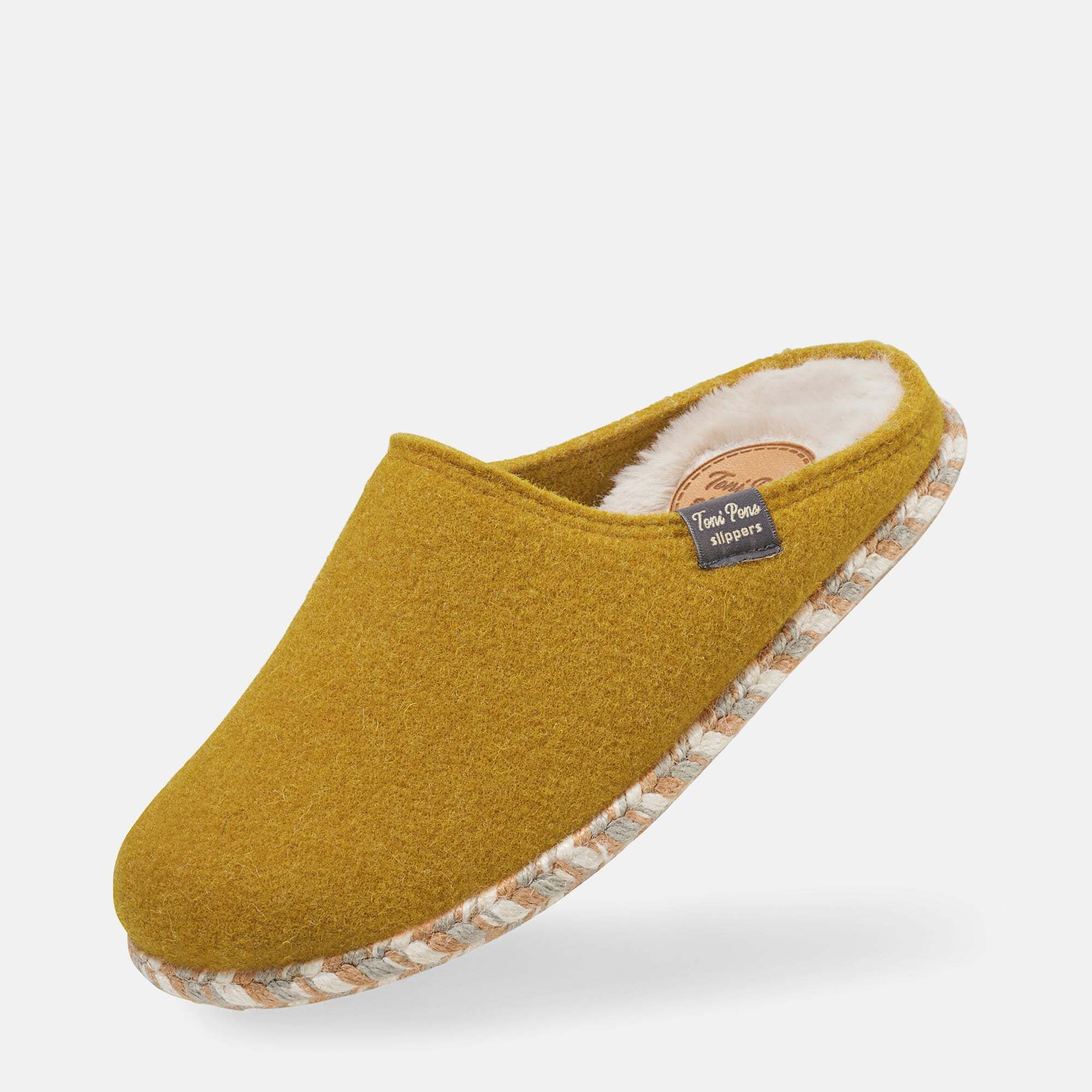 Senffarbener Hausschuh mit weißem Innenfutter und geflochtener Sohle. Label mit Schriftzug. Schuh leicht schräg.