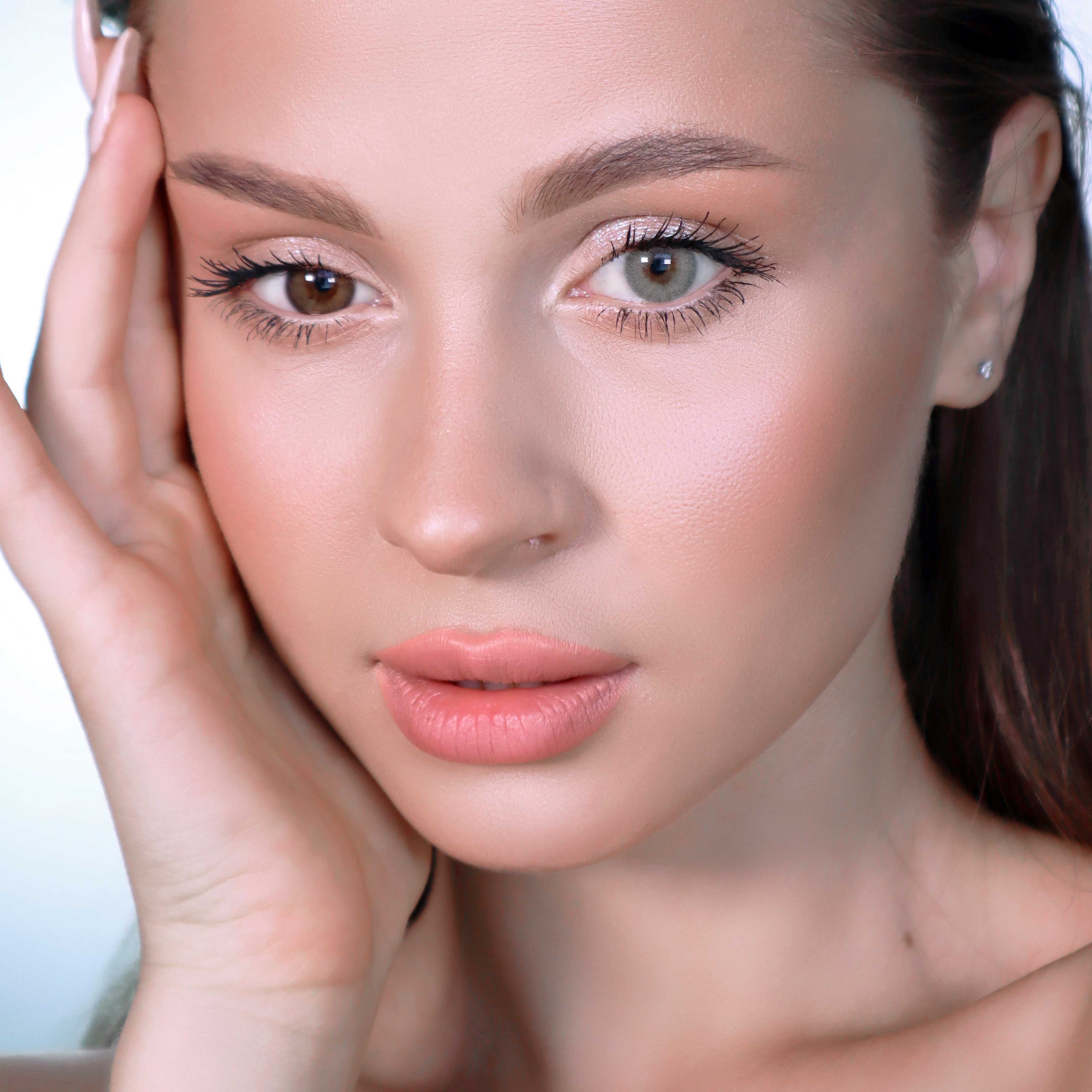 Porträt einer Frau mit unterschiedlich farbigen Augen. Ein Auge ist braun, das andere grünlich-grau. Sie berührt ihr Gesicht.