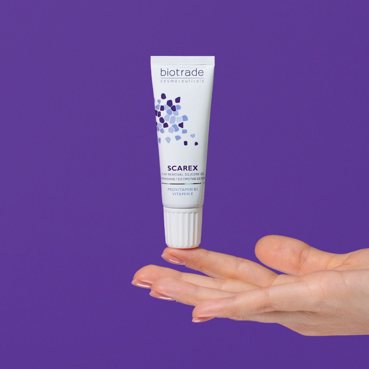 Weiß-blaue Tube mit Produktname und Logo. Wird von einer Hand gehalten, vor violettem Hintergrund.
