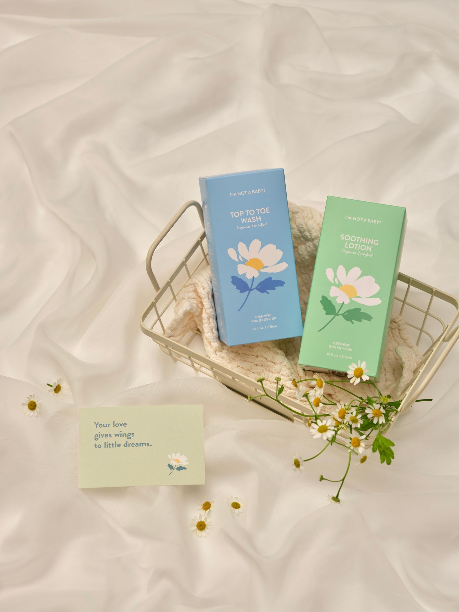 Zwei Schachteln mit floralen Motiven in einem Drahtkorb. Aufschrift: I'm NOT A BABY. Daneben eine Karte mit Text und Gänseblümchen.