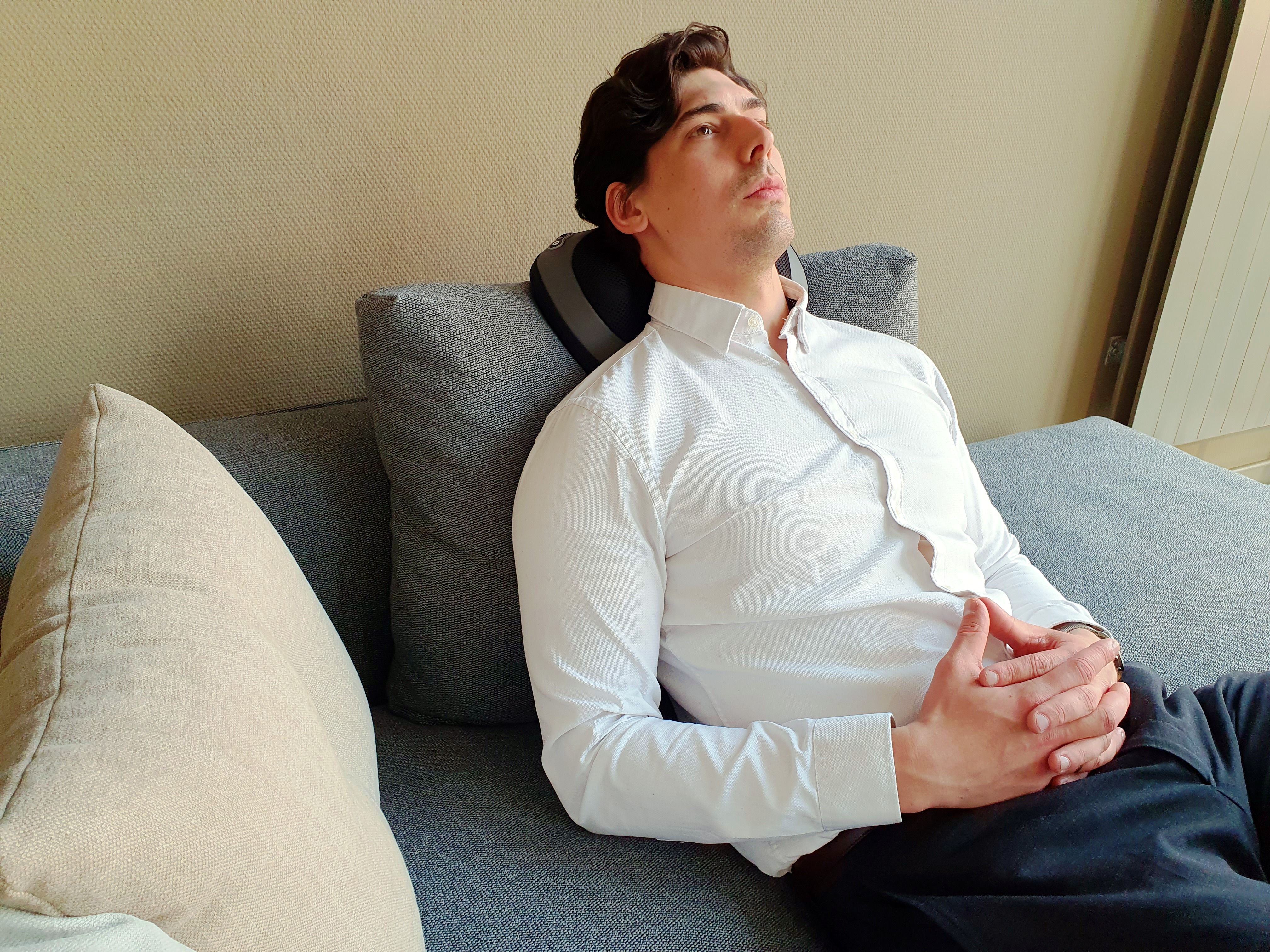 Mann liegt auf Couch, Kopfstütze. Graue Couch, weißes Hemd. Entspannte Haltung. Hintergrund: Wand, Fenster.