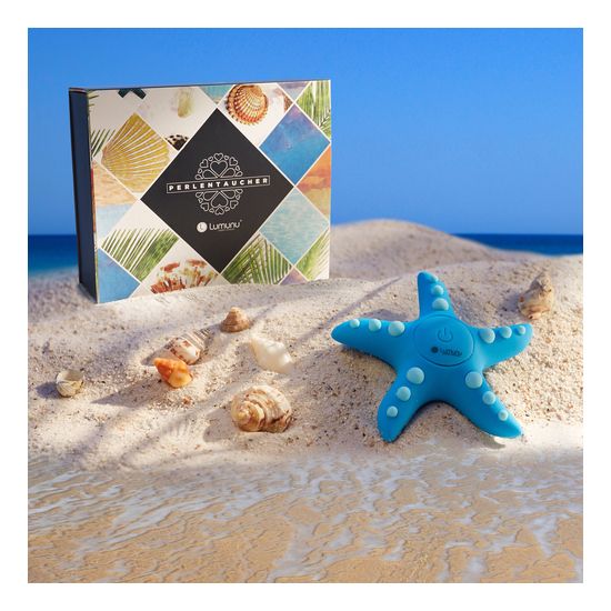 Auflegevibrator in Seesternform, Verpackung und Muscheln auf Sand. Verpackung mit Logo und Schriftzug 'Perlentaucher'.