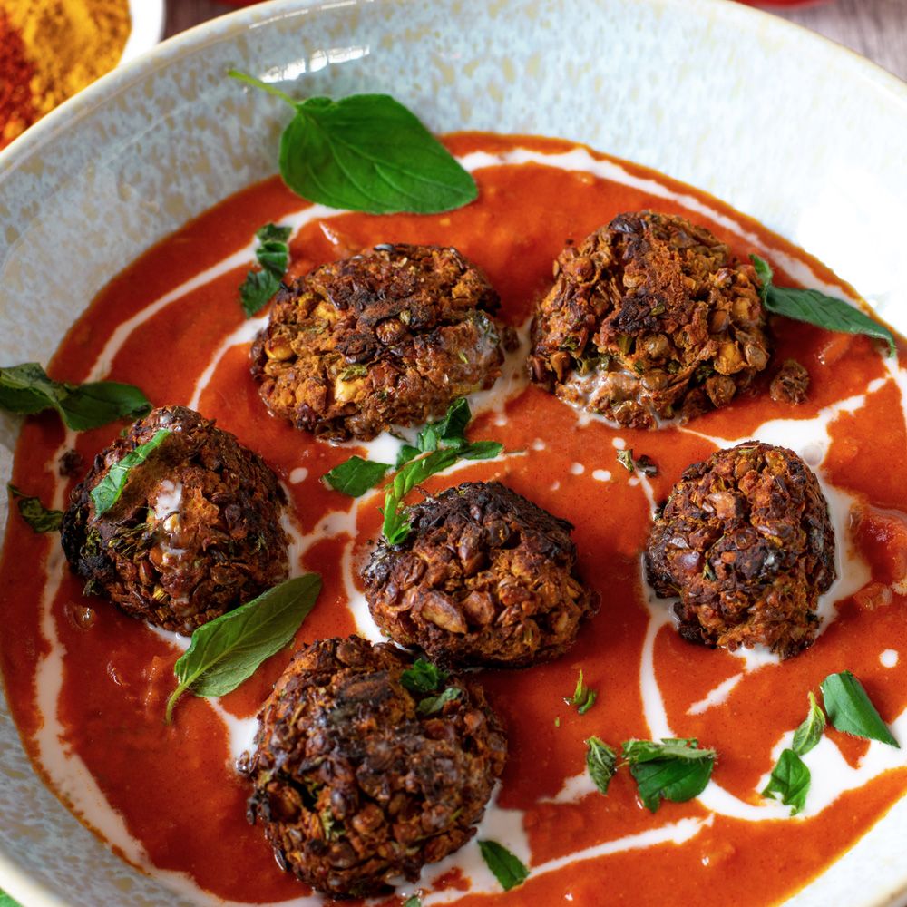 Sechs gebratene Bällchen in einer Schüssel mit roter Sauce und Sahne. Dekoriert mit Basilikumblättern.