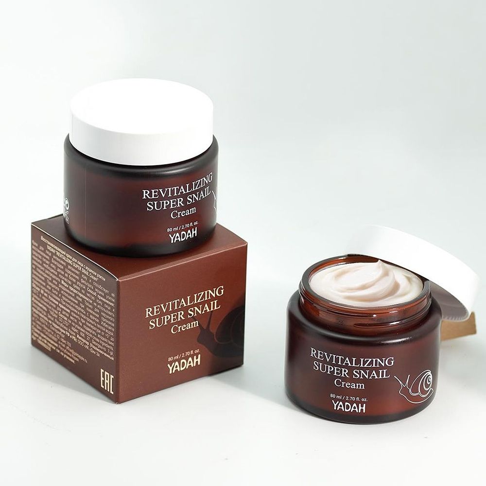 Zwei braune Creme-Dosen mit weißem Deckel und eine Schachtel. Aufschrift: Revitalizing Super Snail Cream, YADAH. Schnecken-Illustration. Text auf der Schachtel.