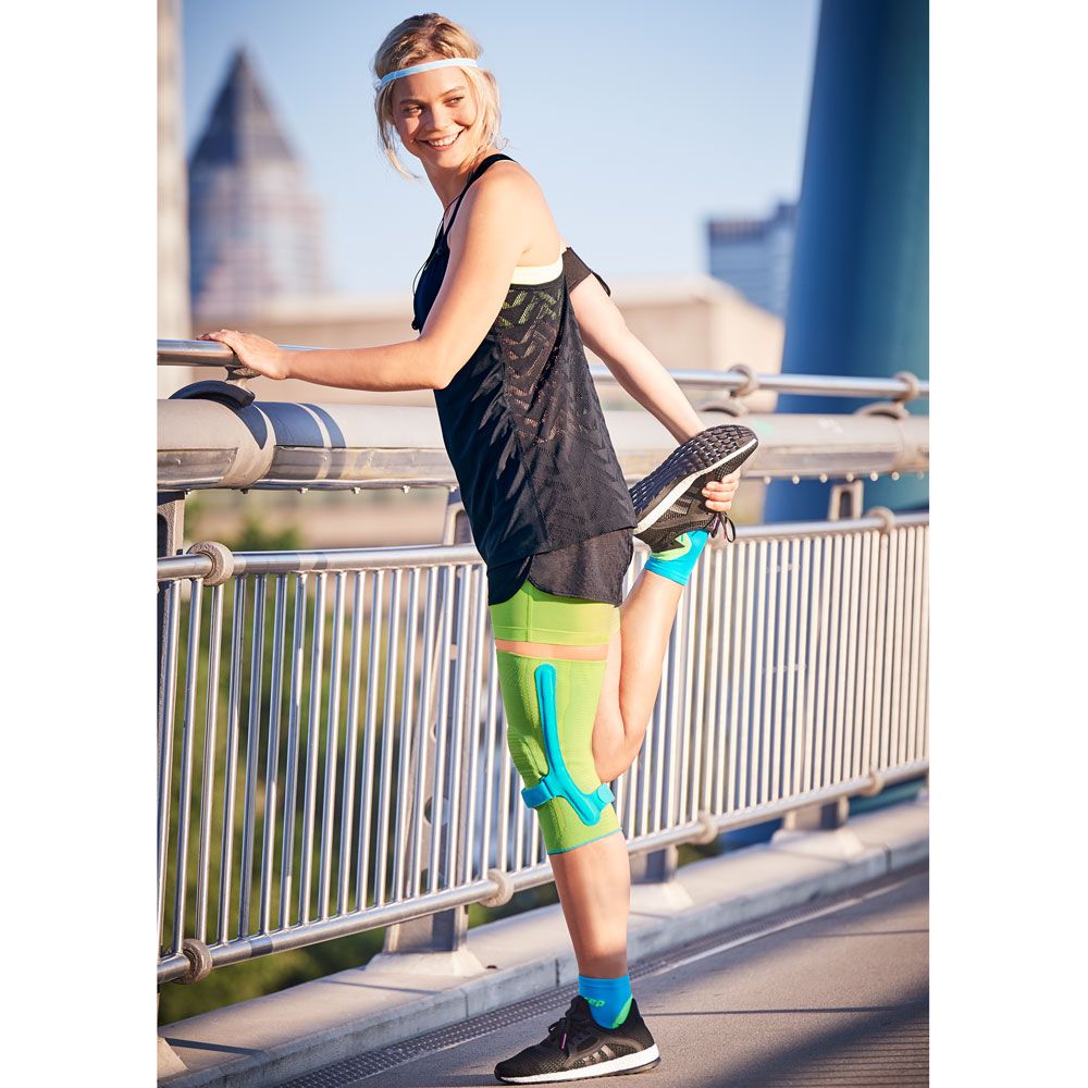 Frau mit Medi Genumedi® PSS Kniebandage dehnt sich auf einer Brücke. Sie trägt Sportkleidung.