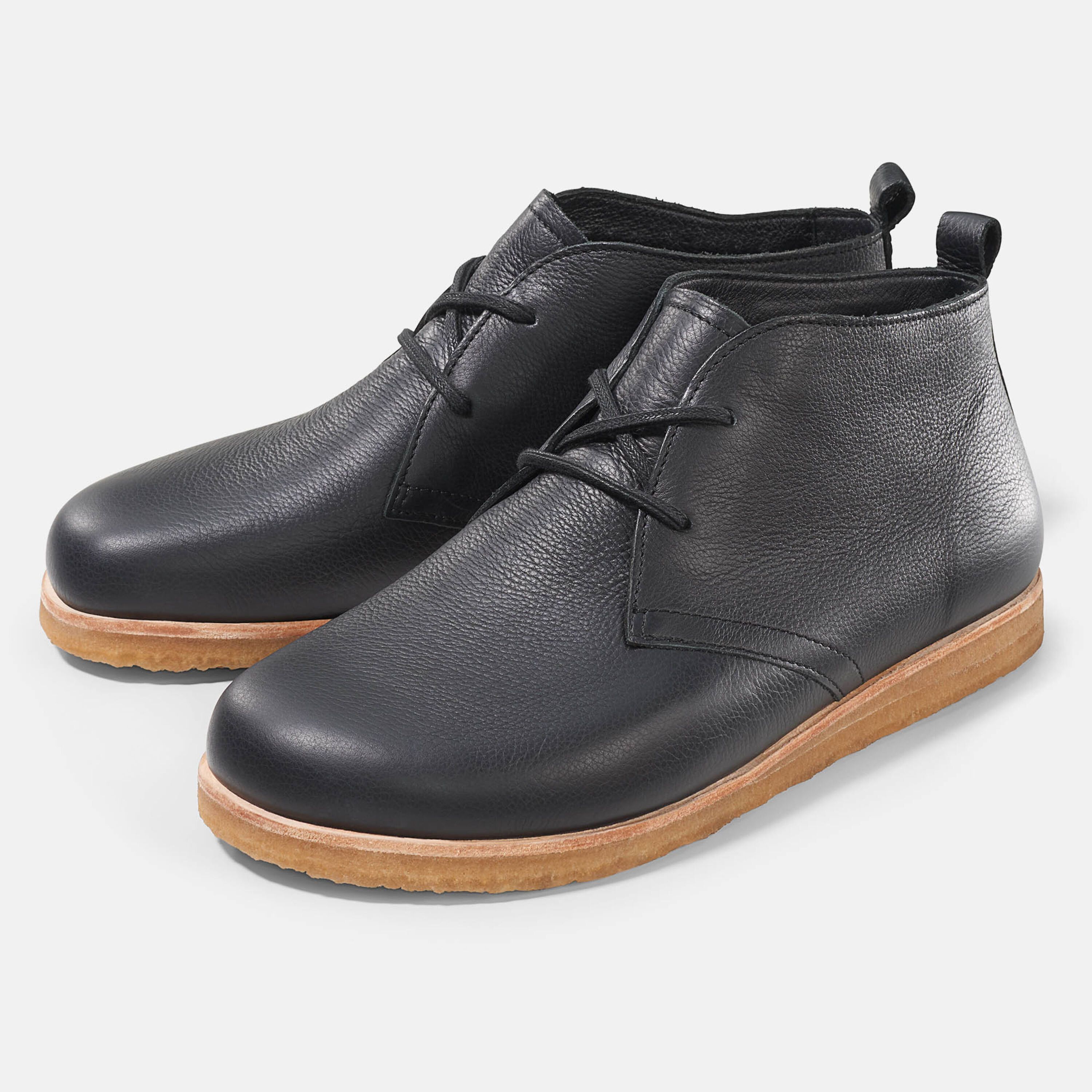 Schwarze Stiefeletten mit Schnürung und heller Sohle. Zwei Schuhe nebeneinander, leicht schräg gestellt.