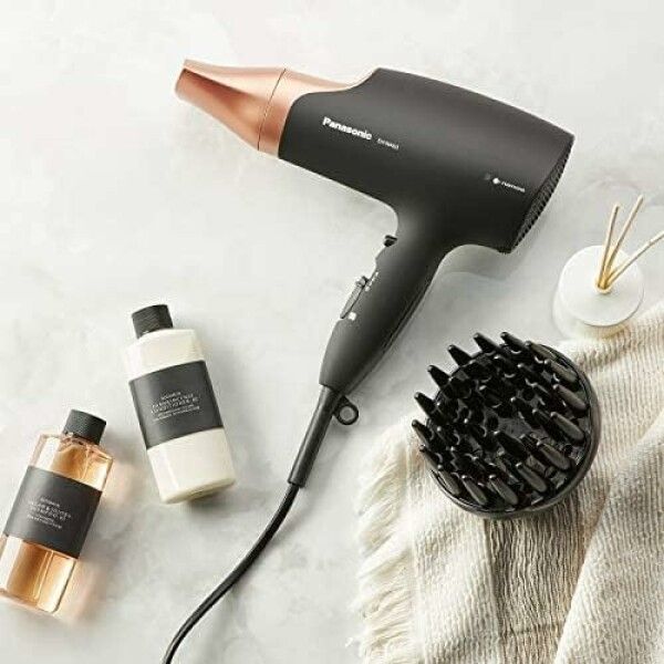 Haartrockner, schwarz mit roségoldfarbener Düse, neben Zubehör und Pflegeprodukten. Marke Panasonic, Modell EH-NA63.
