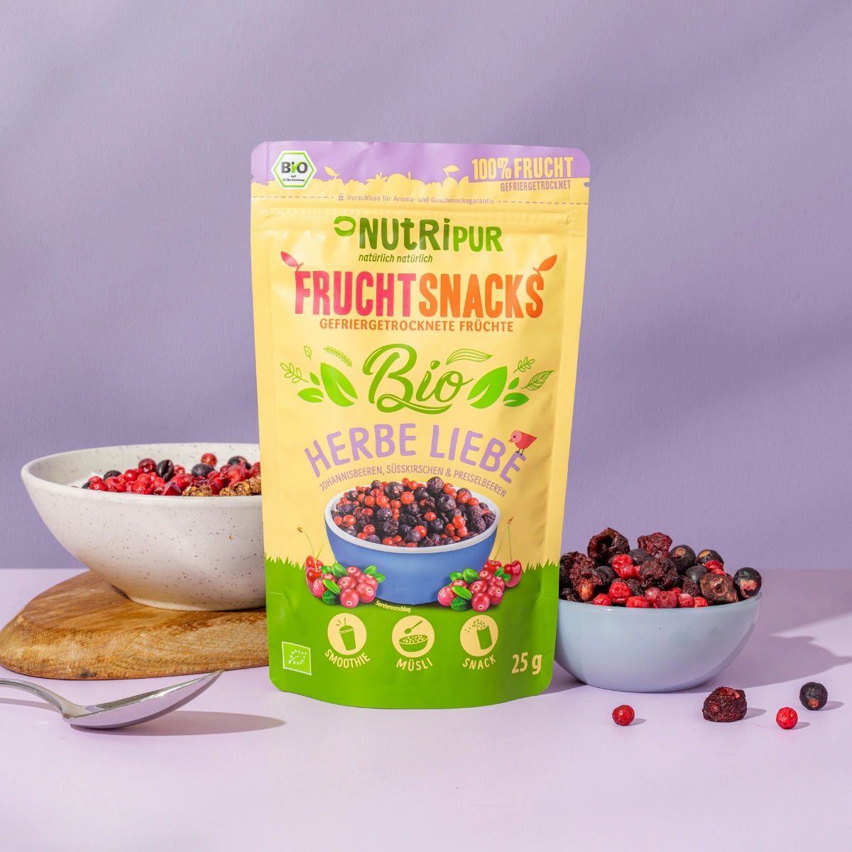 Beutel mit gefriergetrockneten Früchten, neben Schalen mit Früchten. Aufschrift: Bio, Herbe Liebe, 25g.