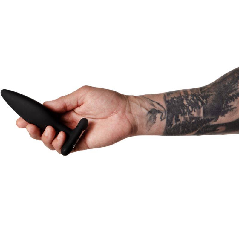 Schwarzer Analplug in einer Hand. Tätowierter Arm. Kegelförmiger Schaft mit T-förmigem Griff.
