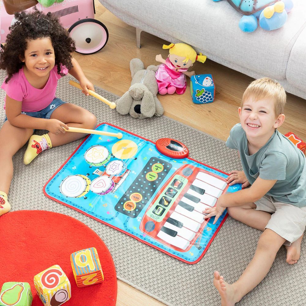 Kinder spielen auf einer blauen Musikmatte mit Trommeln und Klaviertasten. Kinder halten Trommelstöcke. Spielzeug und Kissen im Hintergrund.