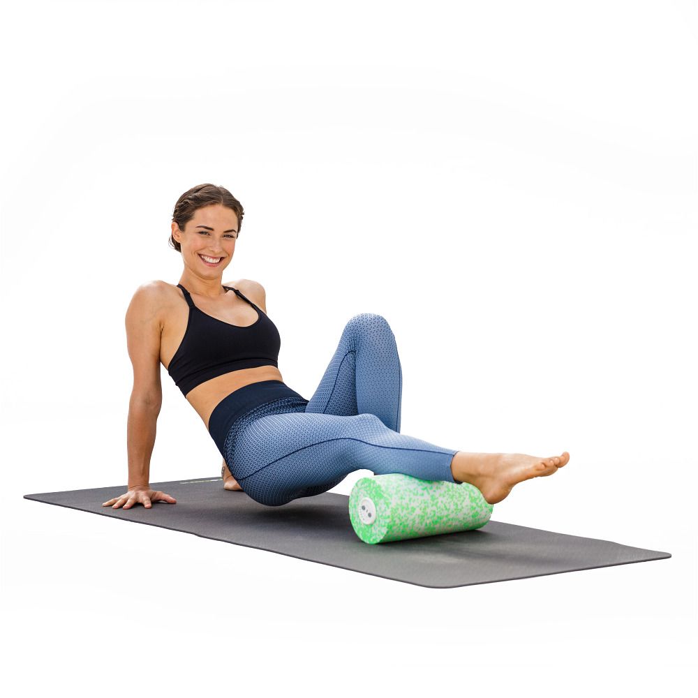 Frau auf Matte mit grünem Faszienroller. Der Roller wird am Fuß verwendet. Schwarze Sportkleidung.