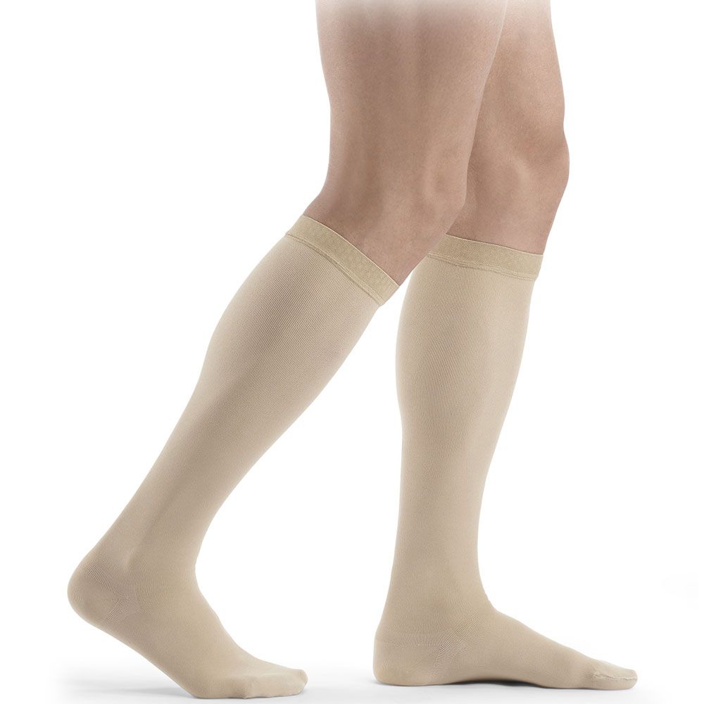 Beige Kompressionsstrümpfe bis zum Knie, mit feinem Rippenmuster am oberen Rand.