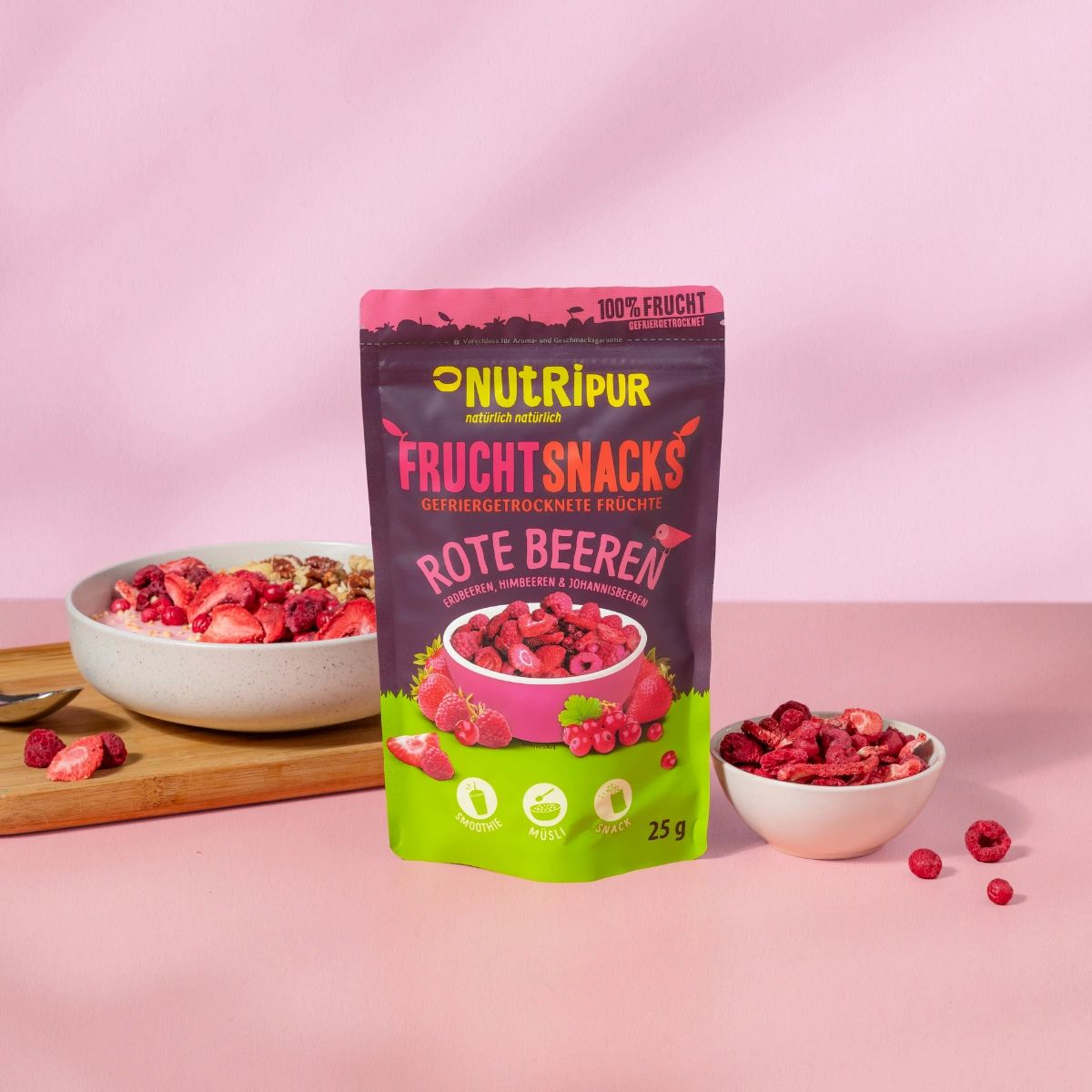 Schale mit Müsli und gefriergetrockneten Früchten. Daneben eine Schale mit Früchten und ein Beutel. 25g.