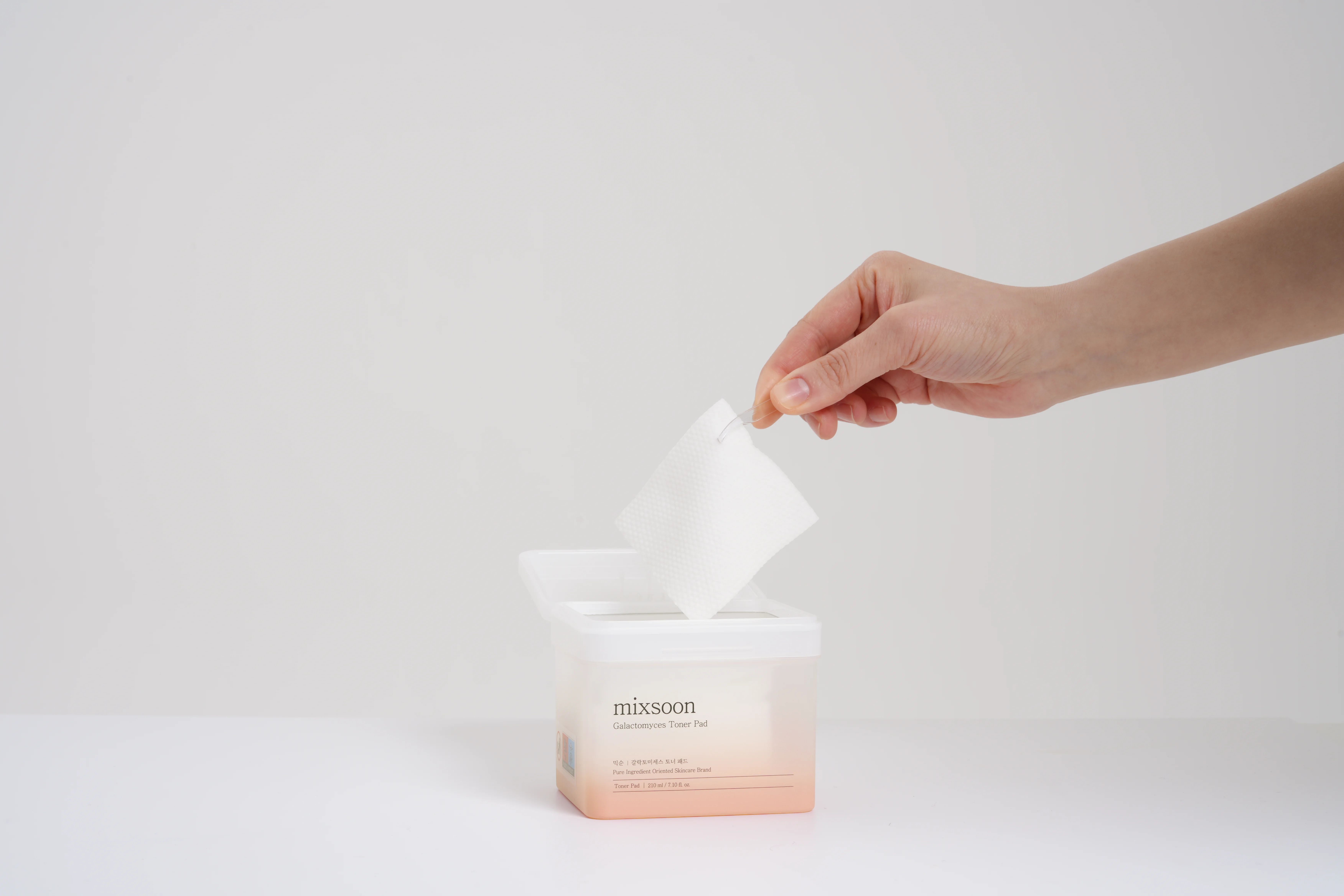 Hand entnimmt Pad aus transparentem Behälter. Behälter mit Aufschrift: mixsoon Galactomyces Toner Pad.