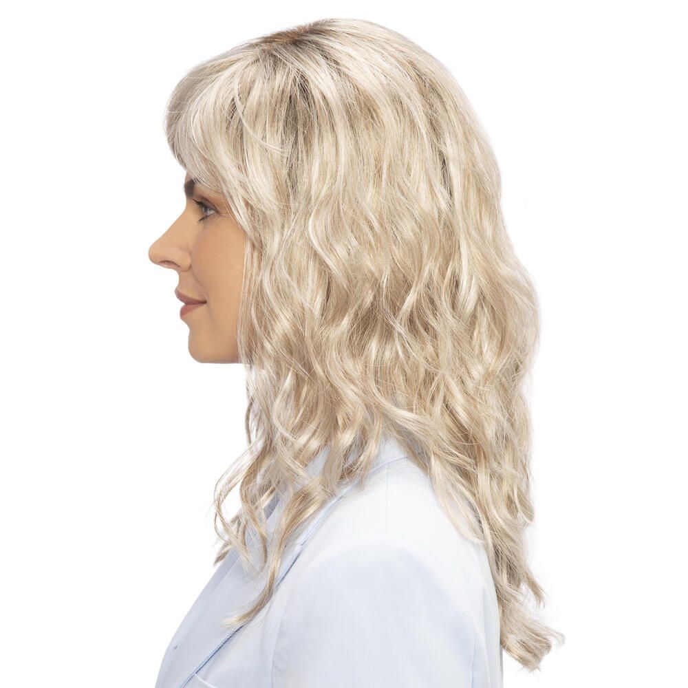 Perücke Kiky von trendhair. Blond, gewellt, mit Pony. Frau trägt hellblaues Jackett. Seitenansicht.