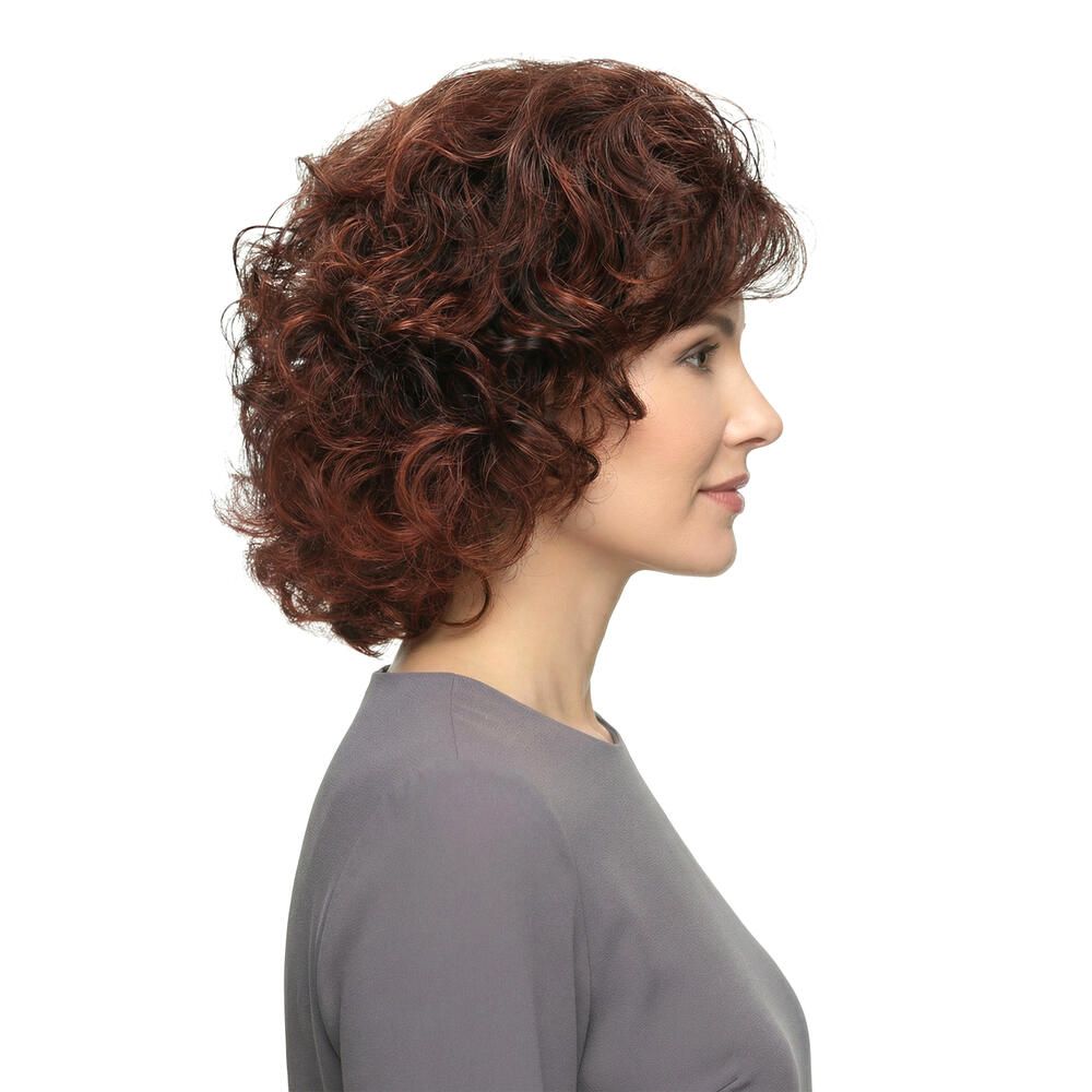 Frau mit brauner, lockiger Perücke. Seitenansicht. Graues Oberteil. Weißer Hintergrund.