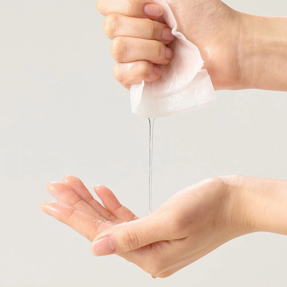 Hände drücken eine Tuchmaske aus, Serum tropft in die Handfläche.