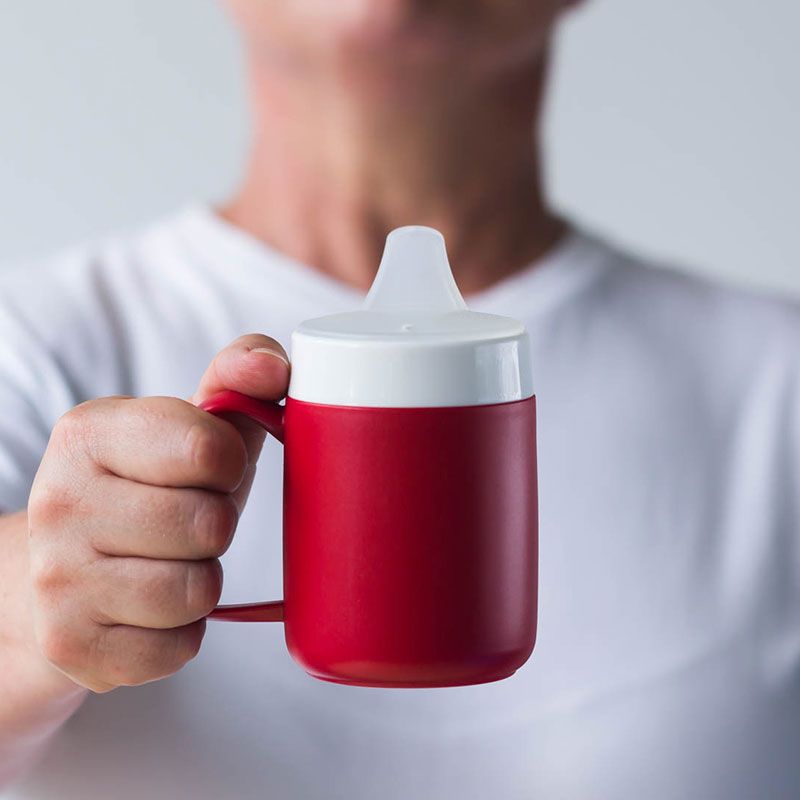 Roter Becher mit weißem Deckel und Trink-Trick-Aufsatz, gehalten von Person.