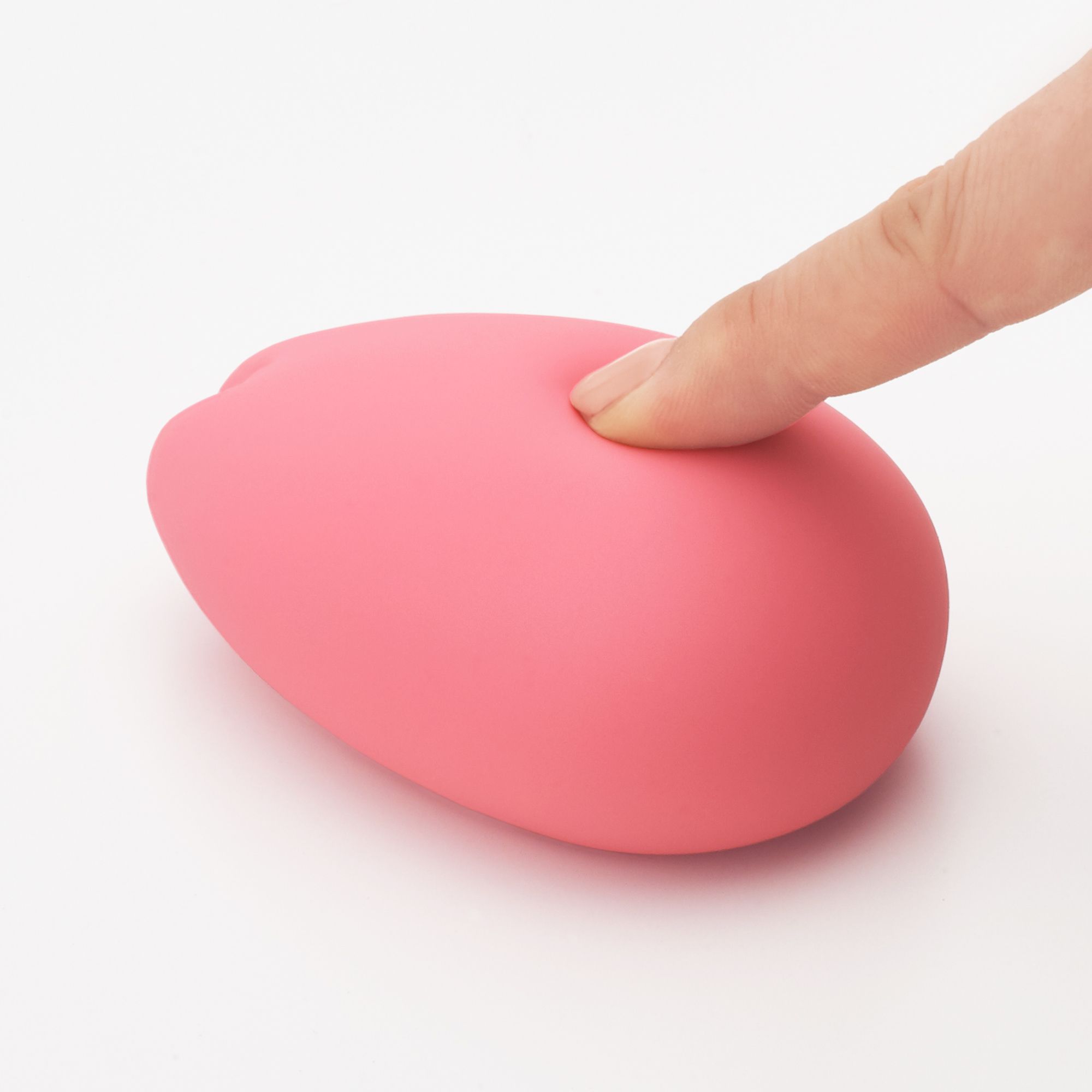 Rosa, tropfenförmiges Produkt. Ein Finger drückt leicht auf die Oberfläche. Auf hellem Hintergrund.