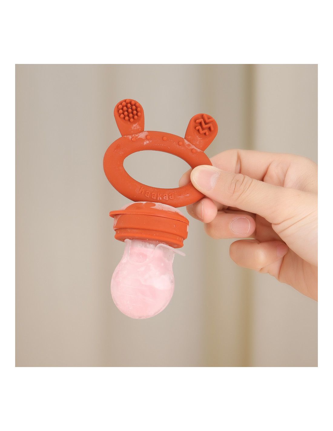 Roter Fruchtsauger mit Fruchtfüllung. Roter Ring mit Logo und zwei Ohren. Hände halten das Produkt.