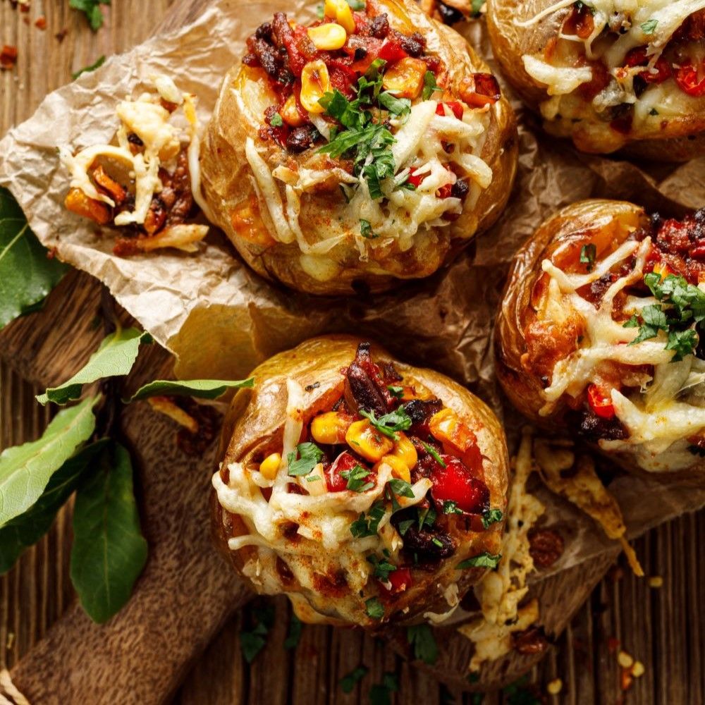 Gebackene Kartoffeln mit Chili con Carne und Käse. Auf Holzbrett. Mais, Bohnen und Kräuter sichtbar.