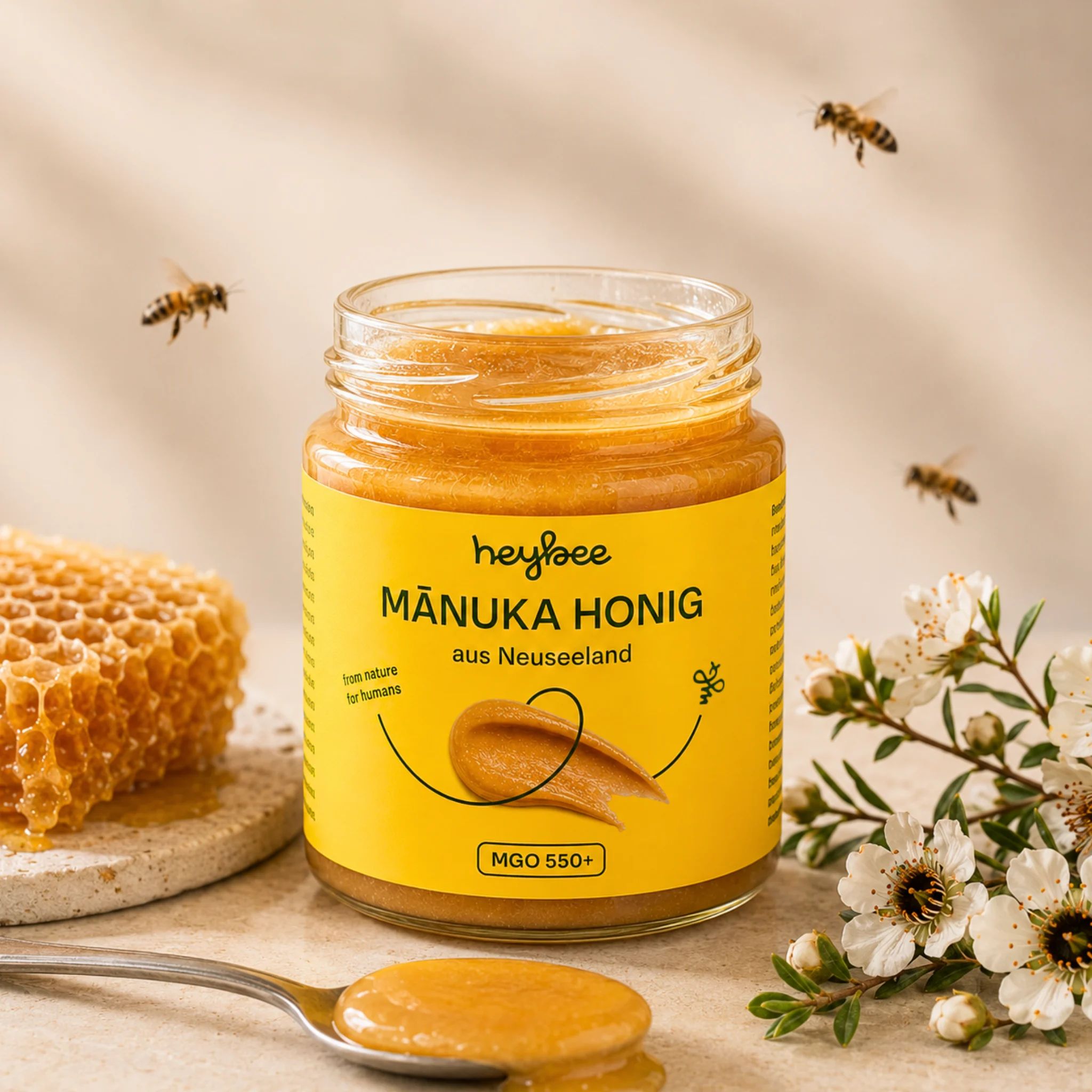 Glas Manuka Honig mit gelbem Etikett, MGO 550+. Daneben Honigwabe und Löffel mit Honig.