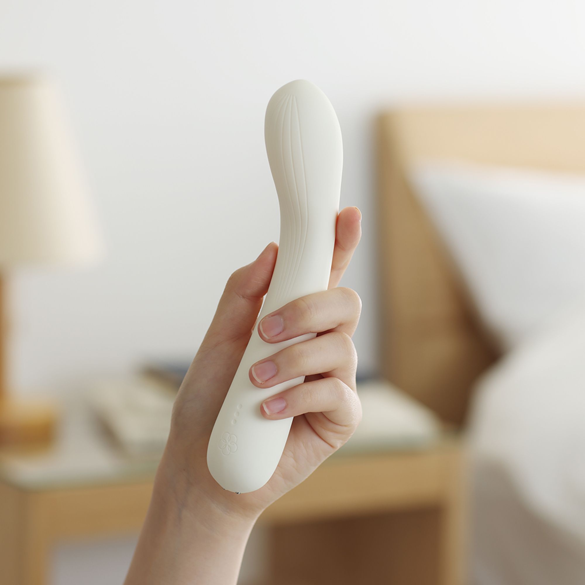 Weißes Wellness-Produkt in einer Hand gehalten. Geschwungene Form. Hintergrund: Schlafzimmer mit Bett und Nachttisch.