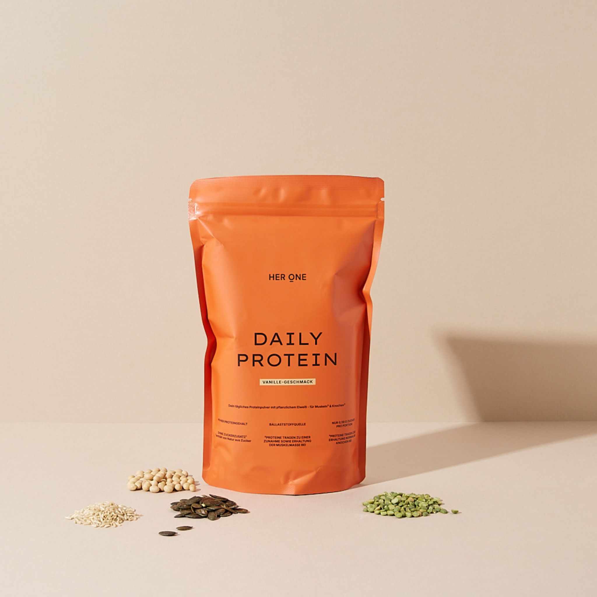 Orangefarbene Protein-Verpackung mit Samen daneben. Aufschrift: "DAILY PROTEIN". Vanille-Geschmack.