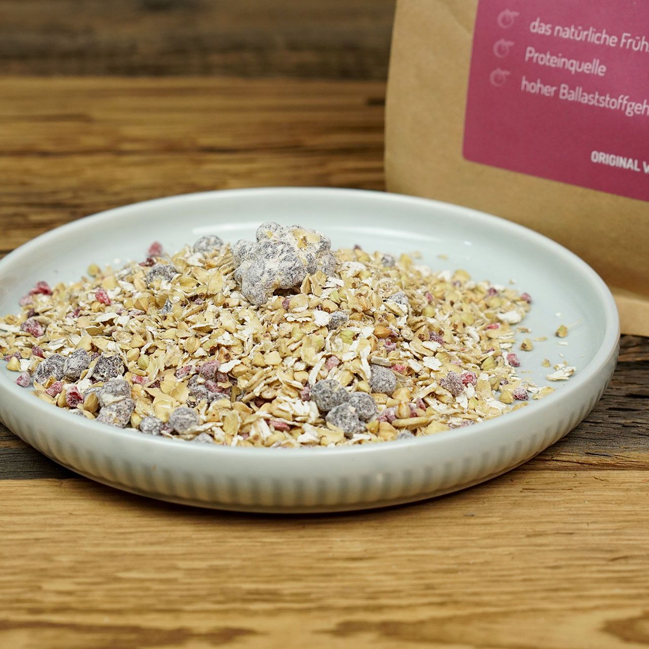 Teller mit Müsli. Müsli mit Beeren auf einem hellgrauen Teller. Im Hintergrund: Verpackung von Wacker Gekeimtes Beerenmüsli Bio.