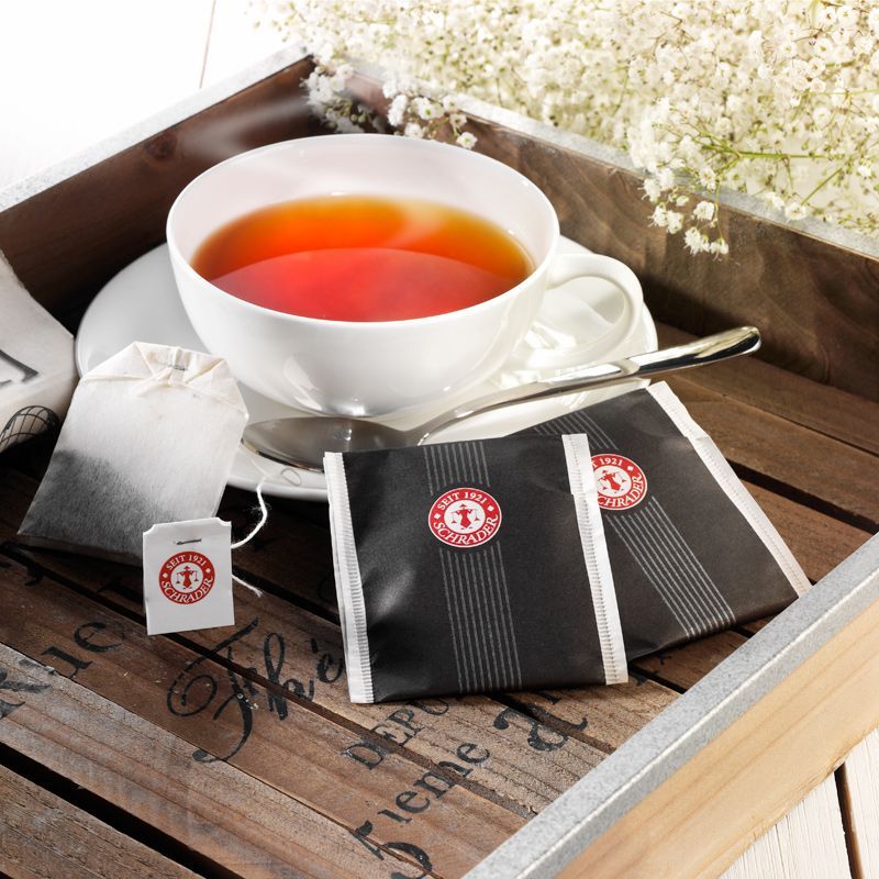 Tasse Tee mit Teebeuteln und Verpackungen auf einem Tablett. Logo auf den Teebeuteln und Verpackungen.