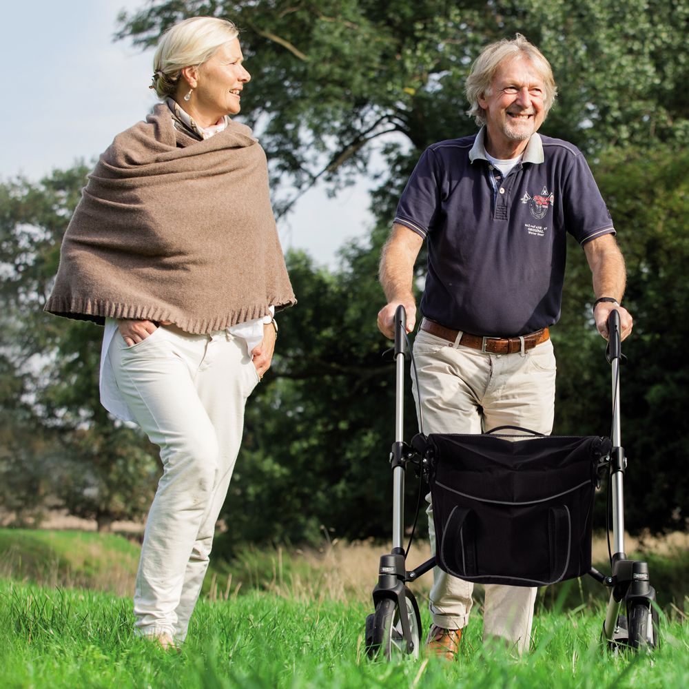 Mann mit Rollator Gemino 60 M im Freien. Frau steht daneben. Beide lächeln. Grüne Wiese im Hintergrund.