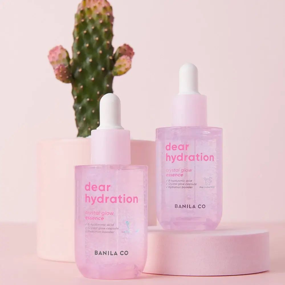 Zwei rosa Serumflaschen mit Pipetten. Aufschrift: dear hydration, crystal glow essence. Marke: BANILA CO. Hintergrund: Pflanze.