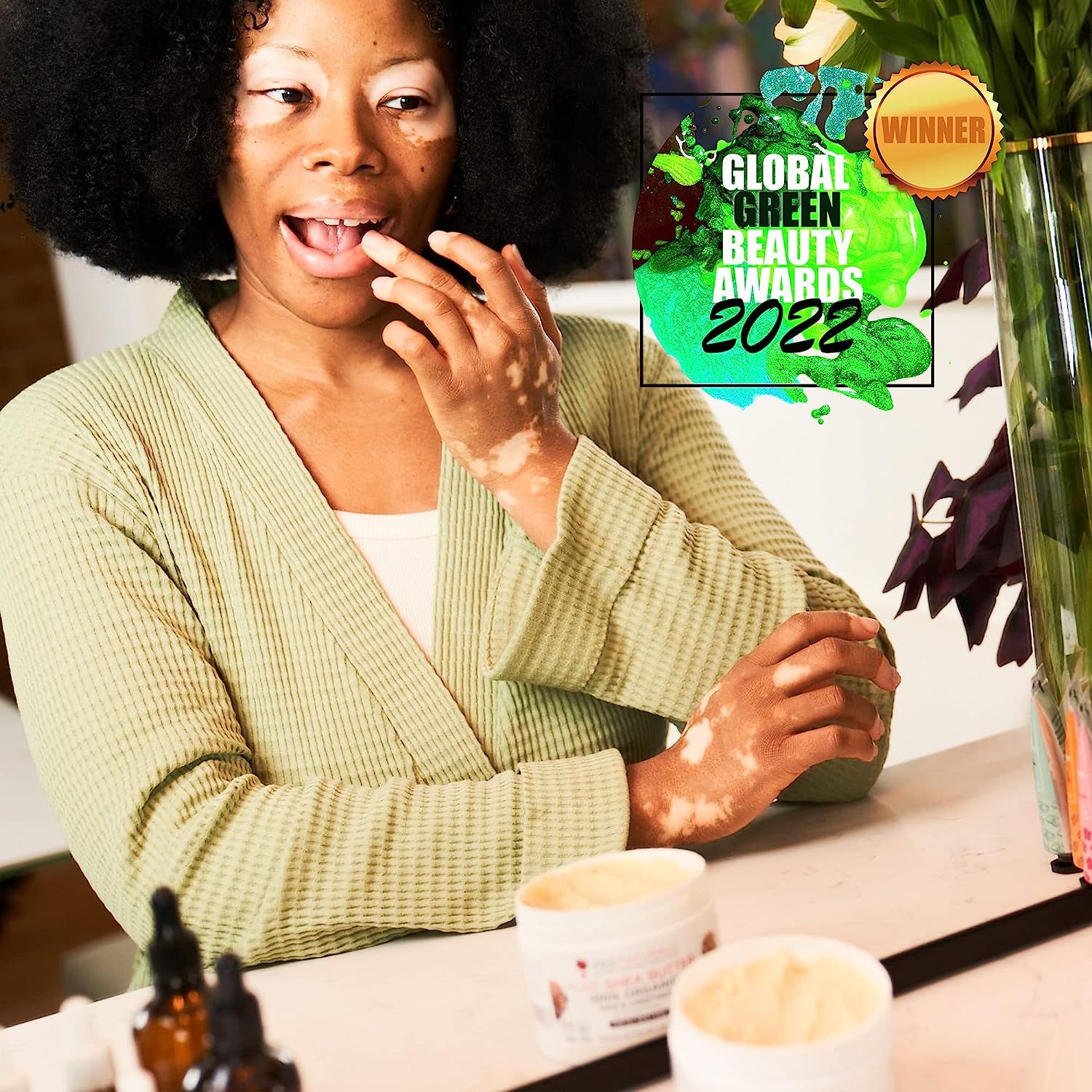 Frau mit Sheabutter-Tiegel. Global Green Beauty Awards 2022. Im Hintergrund Pflanzen und Accessoires.