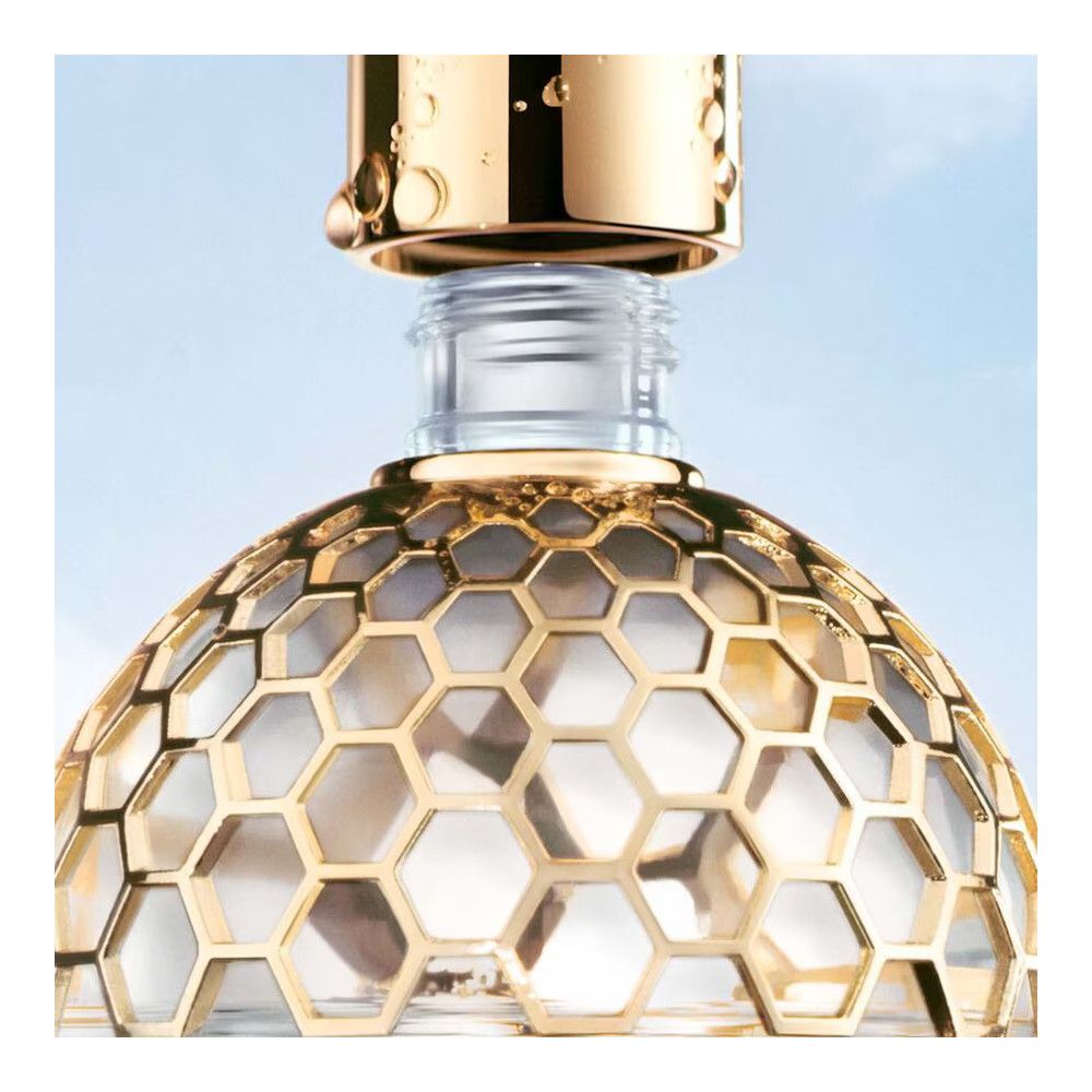 Nahaufnahme des Flakondeckels. Goldfarbene Wabenstruktur. Glasflakon mit Flüssigkeit. Blauer Hintergrund.