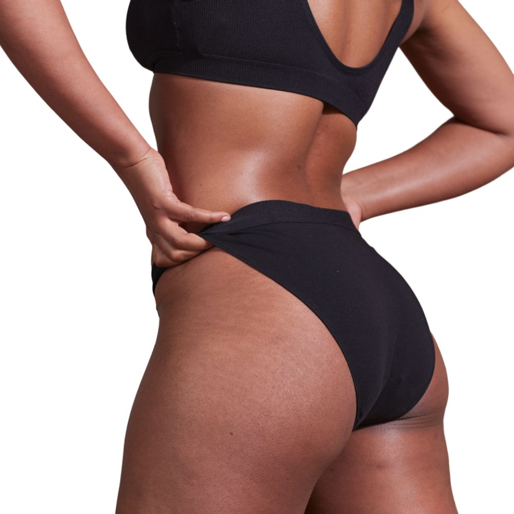 Schwarzer Bikini-Slip aus Bio-Baumwolle. Nahaufnahme einer Person, die den Slip am Bund anfasst.