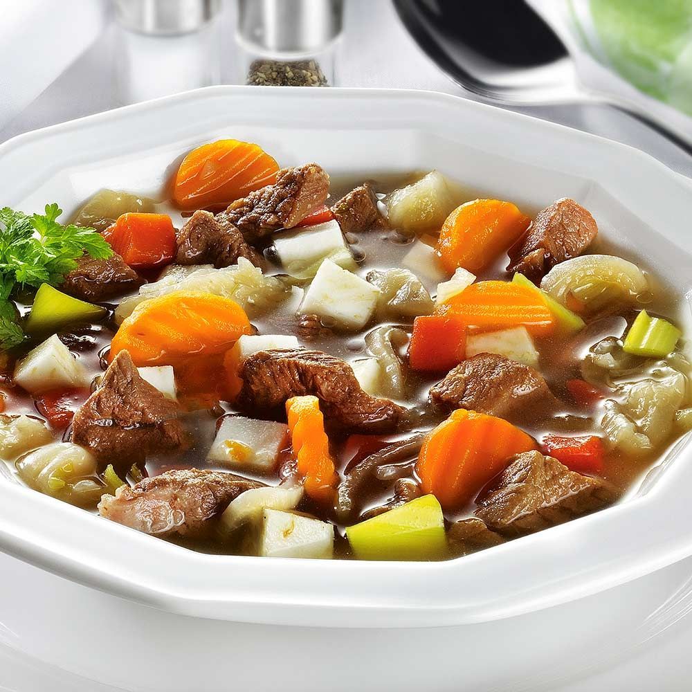 Nahaufnahme von Pichelsteiner Eintopf in weißer Schale. Sichtbar: Fleisch, Gemüse, Brühe.