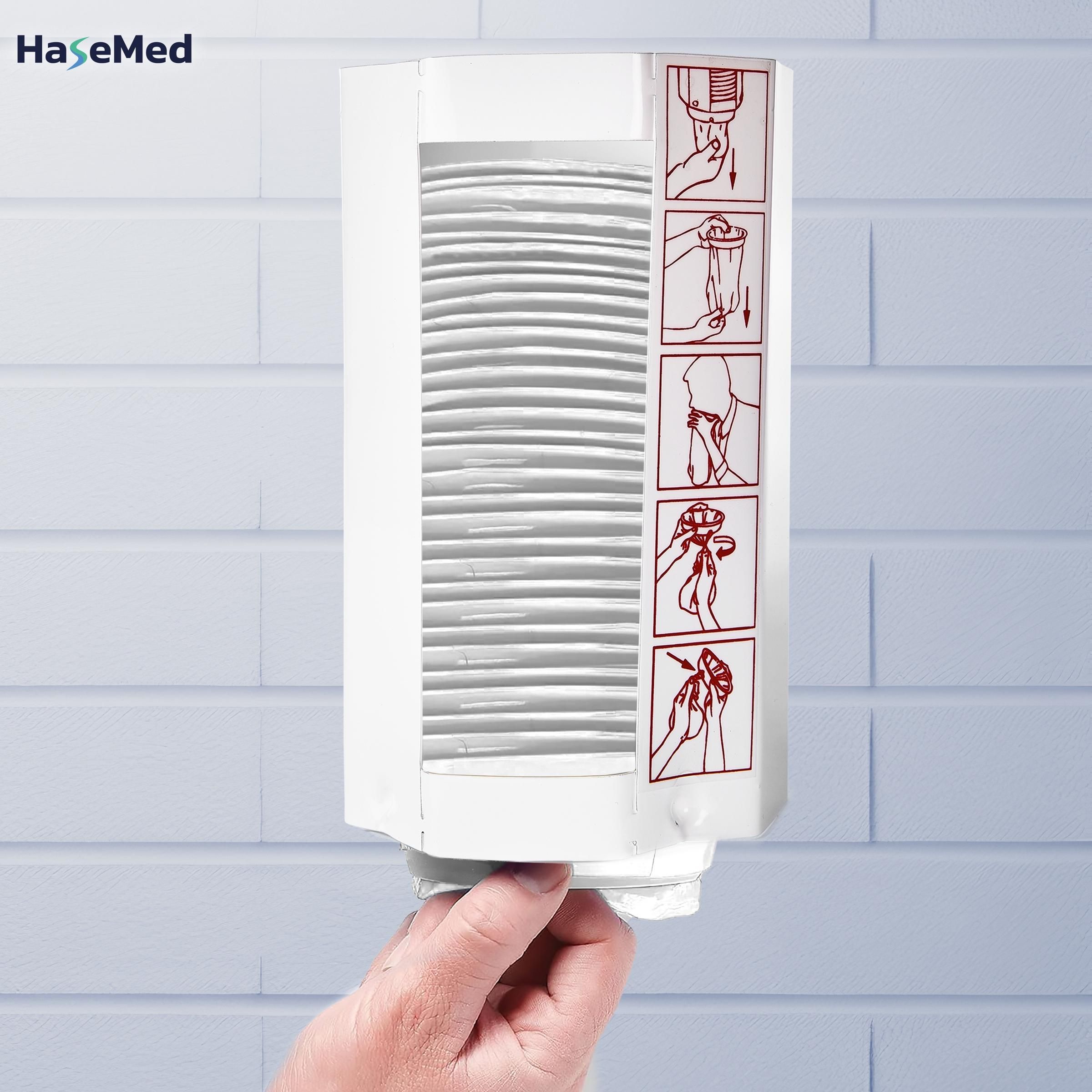 Weißer Metallspender für Spuckbeutel, gefüllt mit Spuckbeuteln. Auf der Seite sind Anweisungen abgebildet. Logo: HaseMed. Hand hält den Spender.