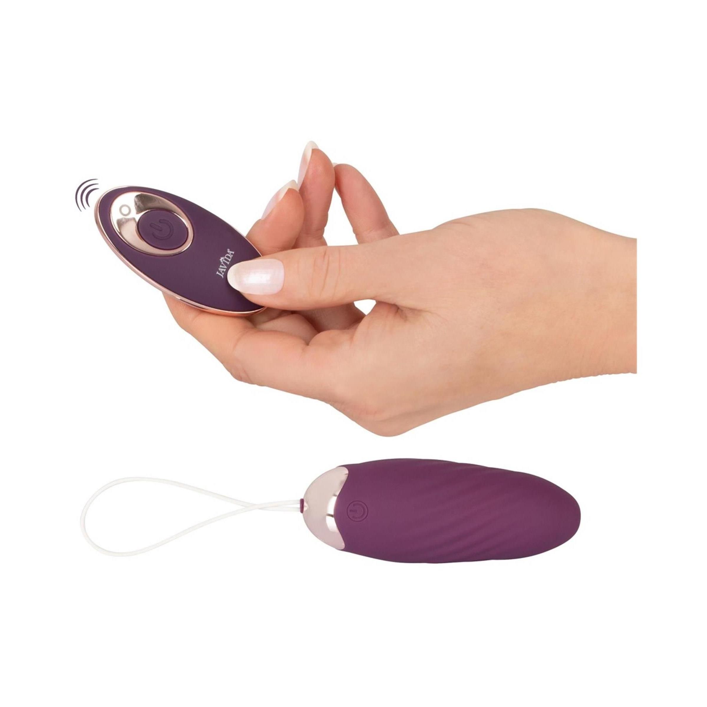 Hand hält Fernbedienung, Javida Shaking Love Ball darunter. Beide oval, lila mit goldfarbenen Akzenten.