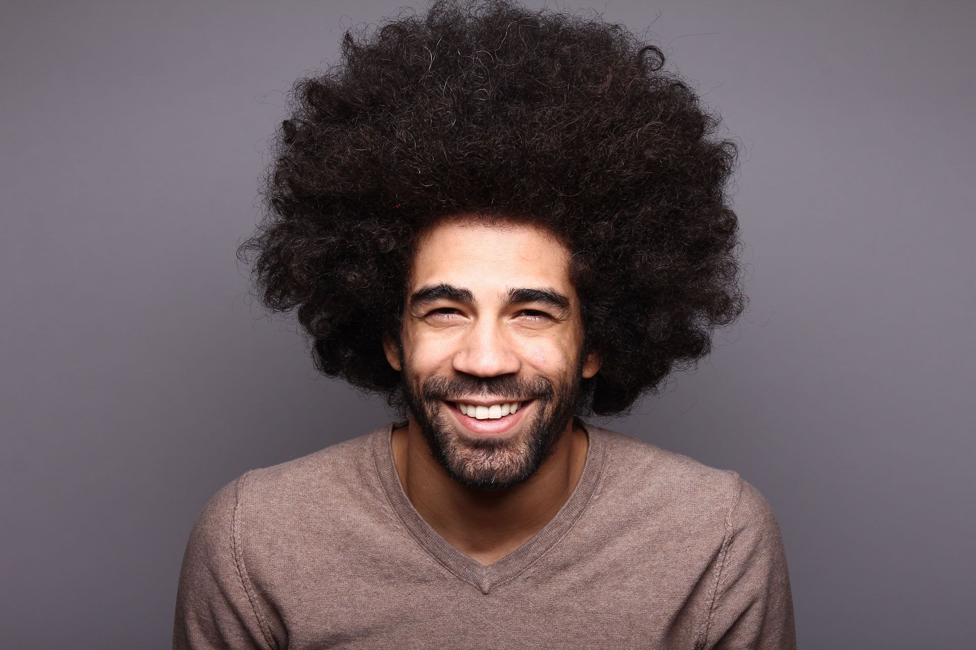 Mann mit voluminösem Afro-Haar lächelt in die Kamera.