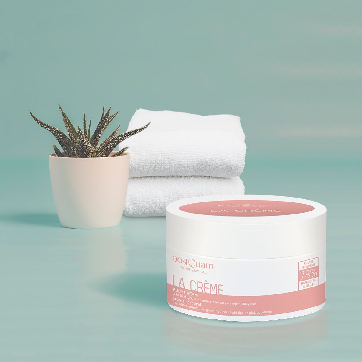 Weißer Tiegel mit rosa Deckel, Aufschrift La Crème und PostQuam. Daneben ein Topf mit Pflanze und Handtücher.