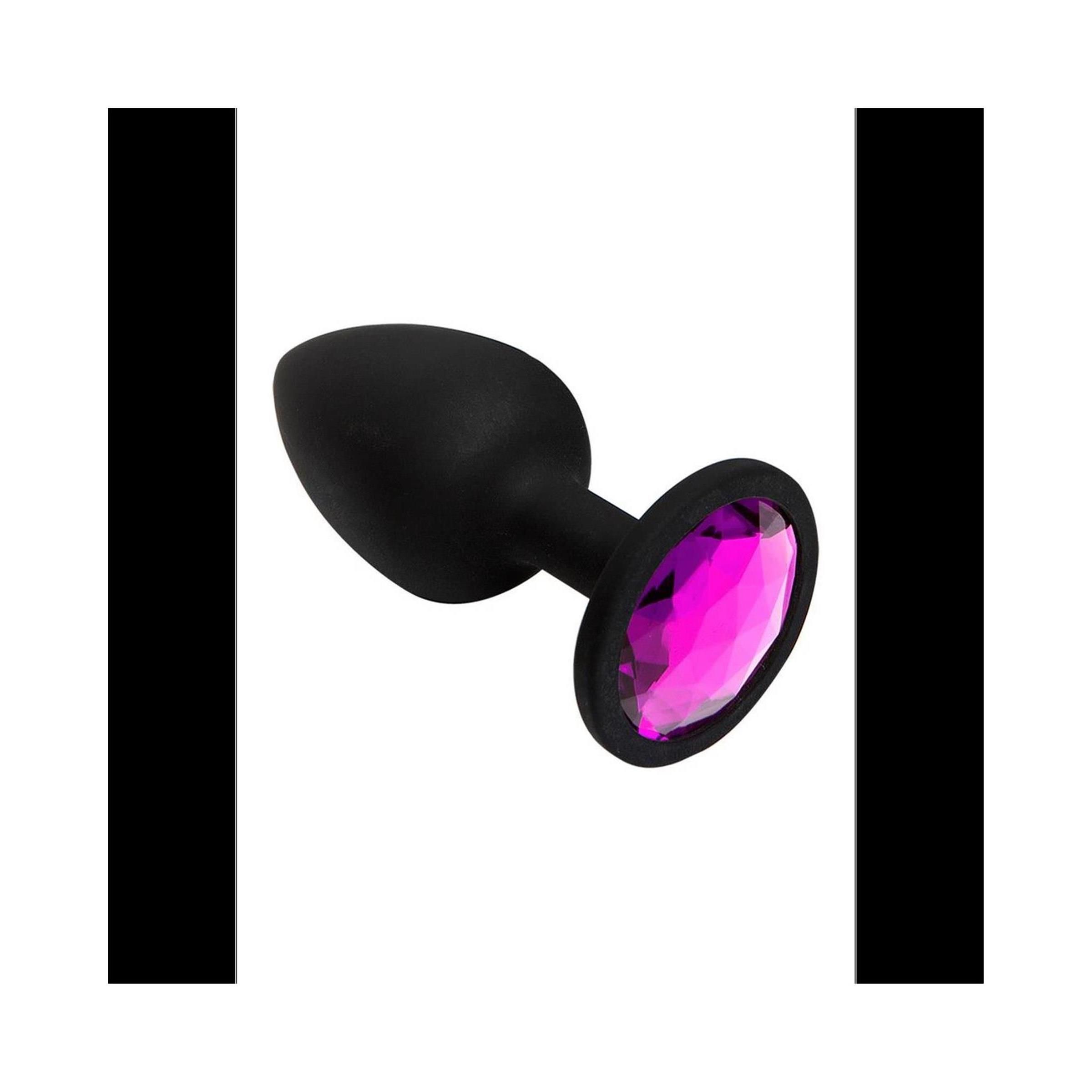 Schwarzer, spatenförmiger Plug mit rosa Schmuckstein an der Basis. Der Plug liegt auf einer weißen Oberfläche.