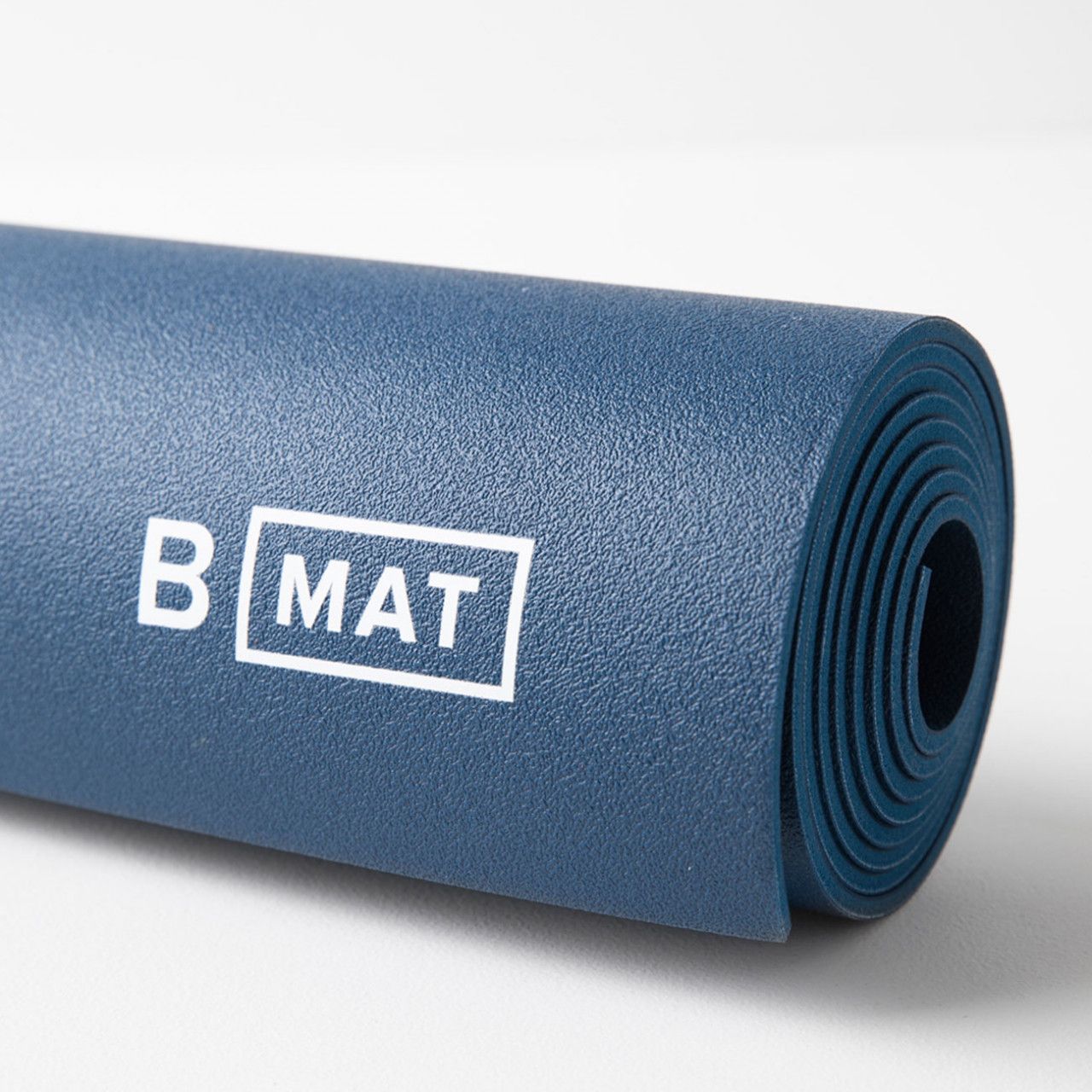Gerollte blaue Yogamatte. Weißer Schriftzug "B MAT" in einem Rechteck. Nahaufnahme.