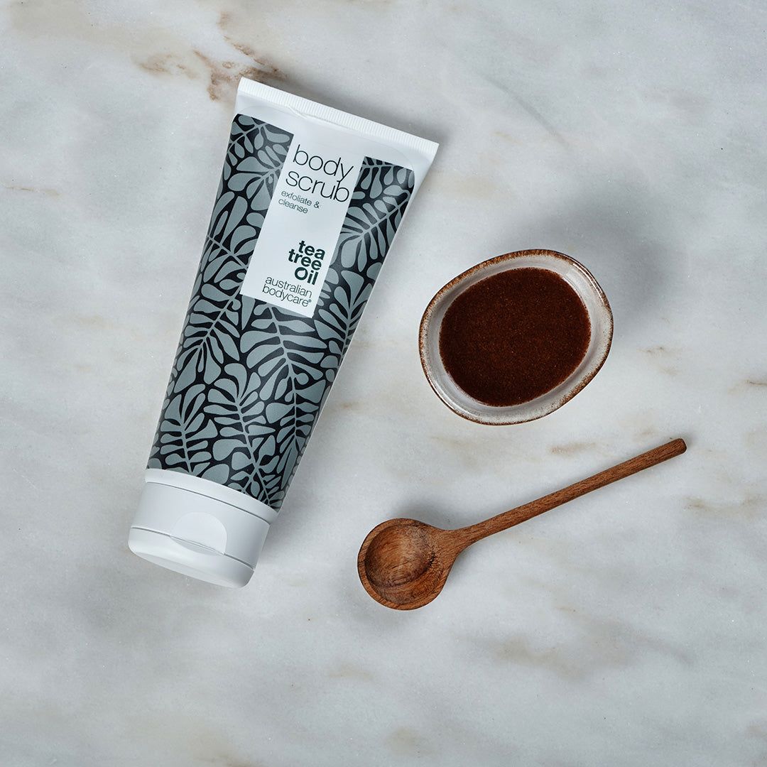 Body Scrub Tube, Schüssel und Löffel. Weiße Tube mit grauen Blättern. Text: Tea Tree Oil, Australian Bodycare. Braunes Produkt.