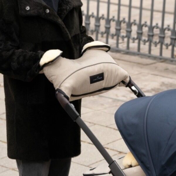 Person hält Handwärmer an einem Kinderwagen. Beige Handwärmer mit schwarzem Rand. Werner Christ Label.