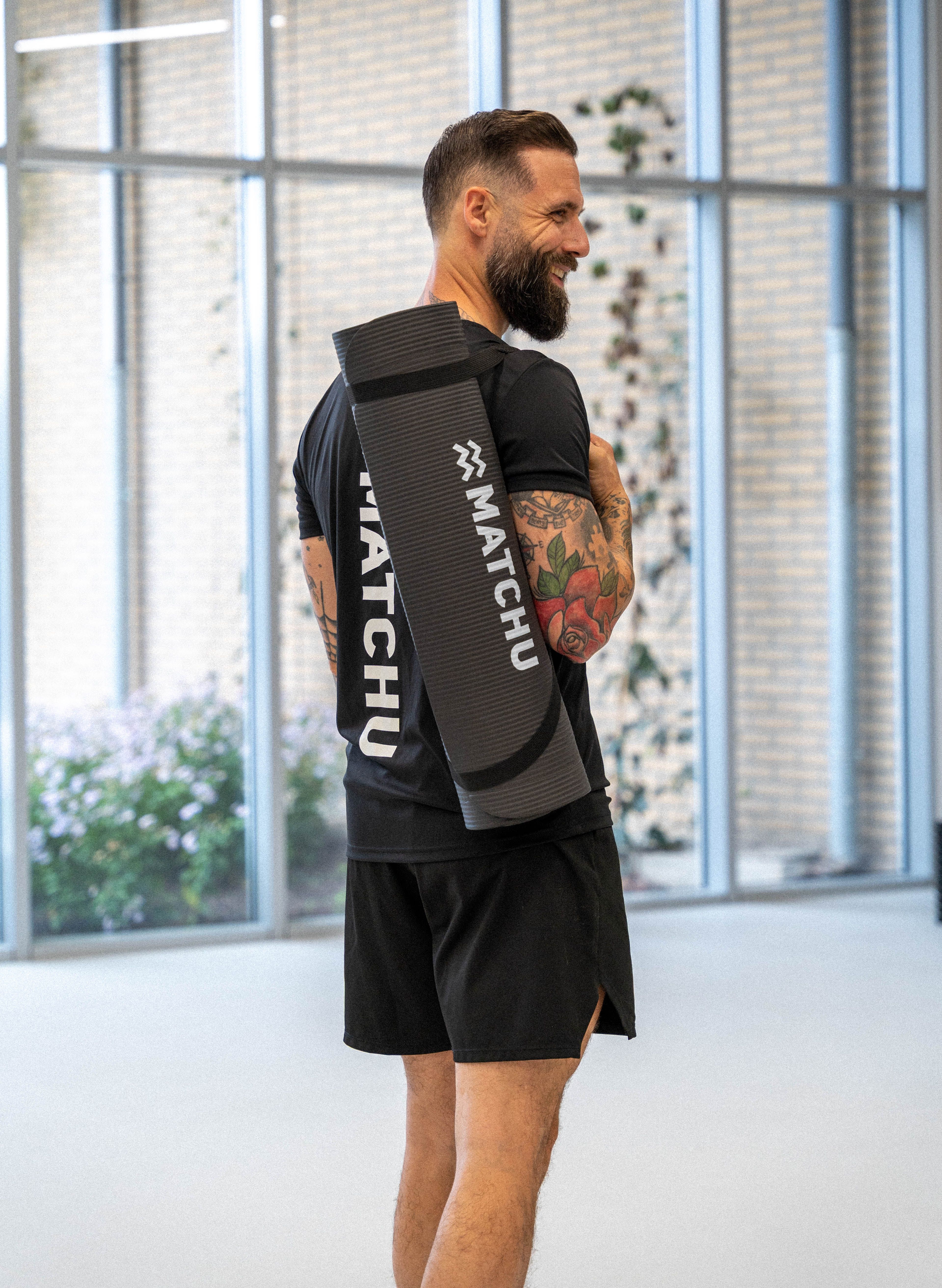 Mann mit schwarzer Yogamatte über der Schulter. Matte mit "MATCHU"-Logo.