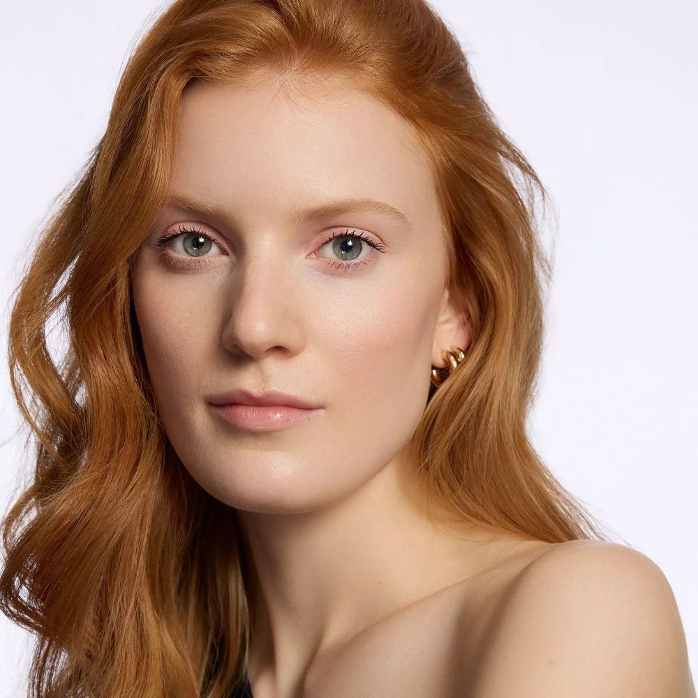 Porträt einer Frau mit rotem Haar. Sie trägt Ohrringe und hat einen natürlichen Teint.